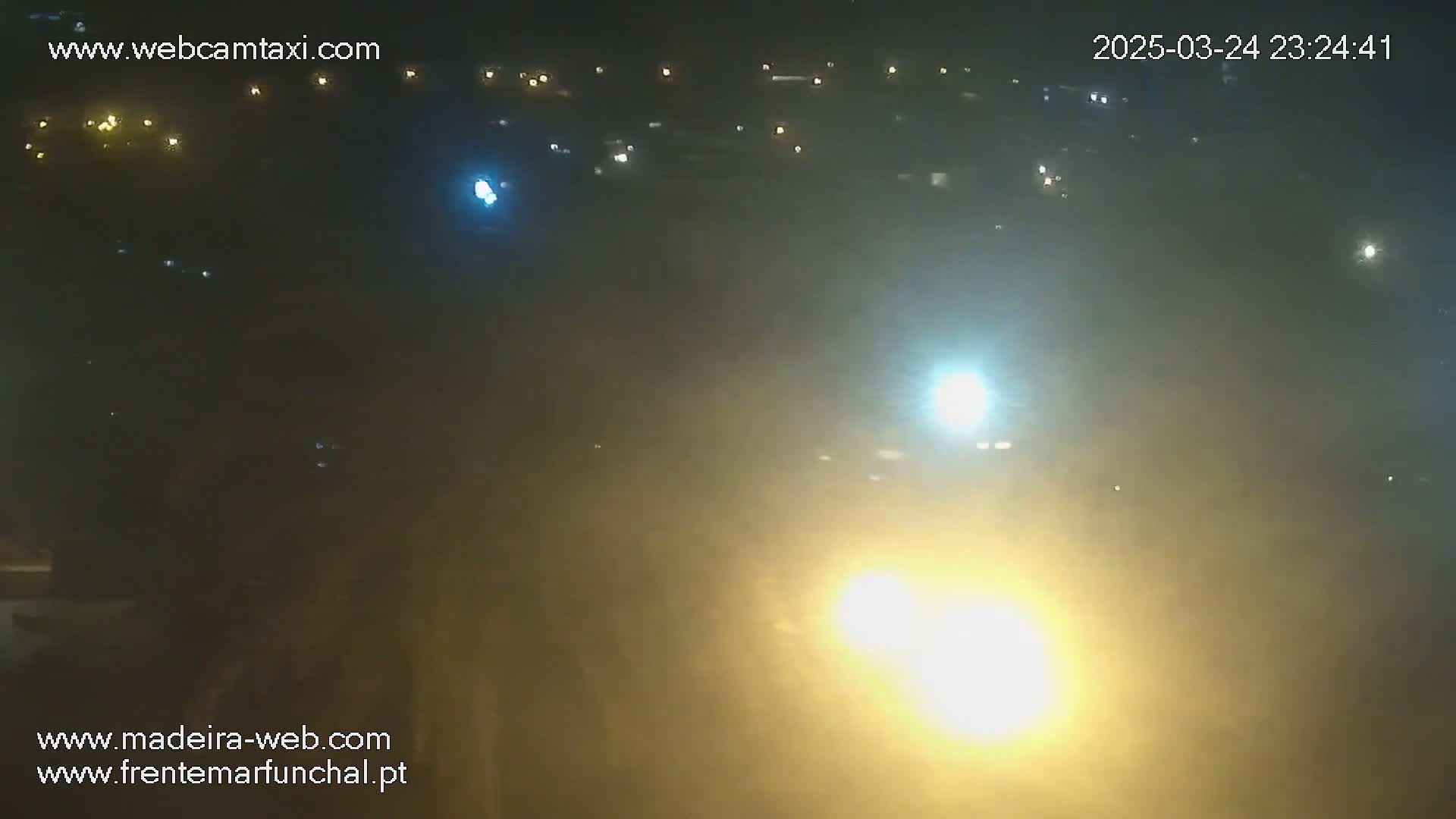 A hazy, nighttime view shows distant lights from a town or city under a somewhat foggy sky.