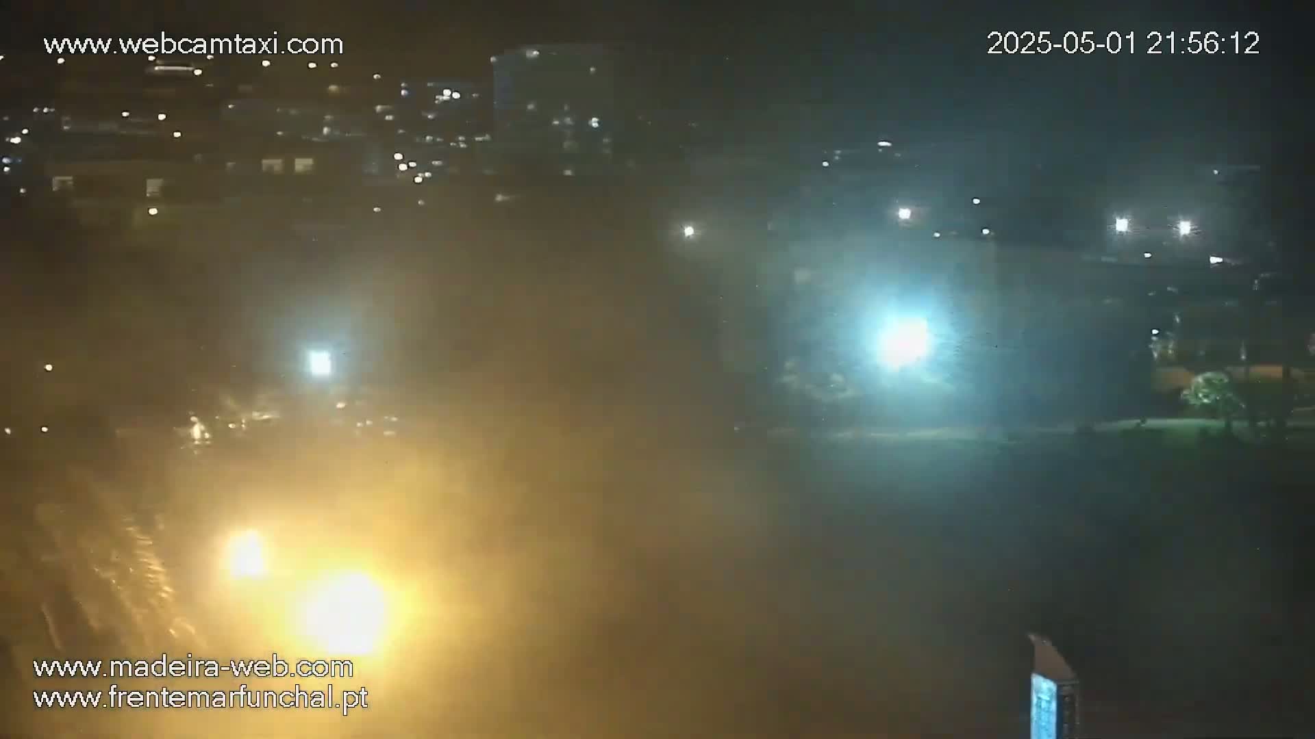 A nighttime, hazy or foggy scene shows distant lights from buildings and vehicles, with brighter lights closer to the foreground.