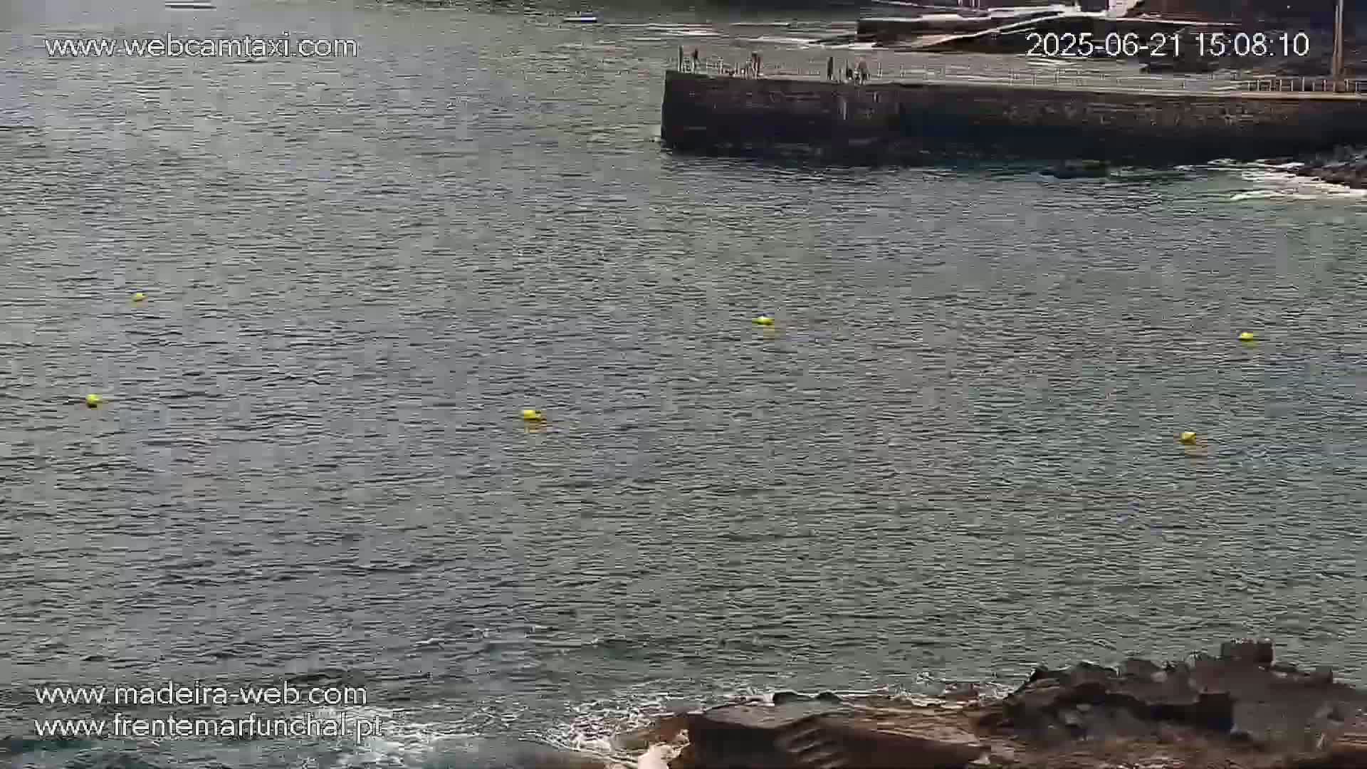 A calm body of water with several yellow buoys and a stone structure in the background.
