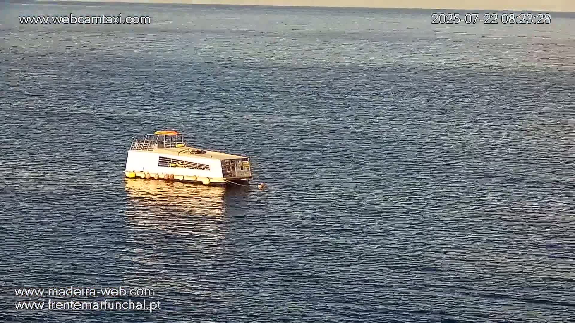 A small, white passenger boat is moored in calm, dark-blue water.