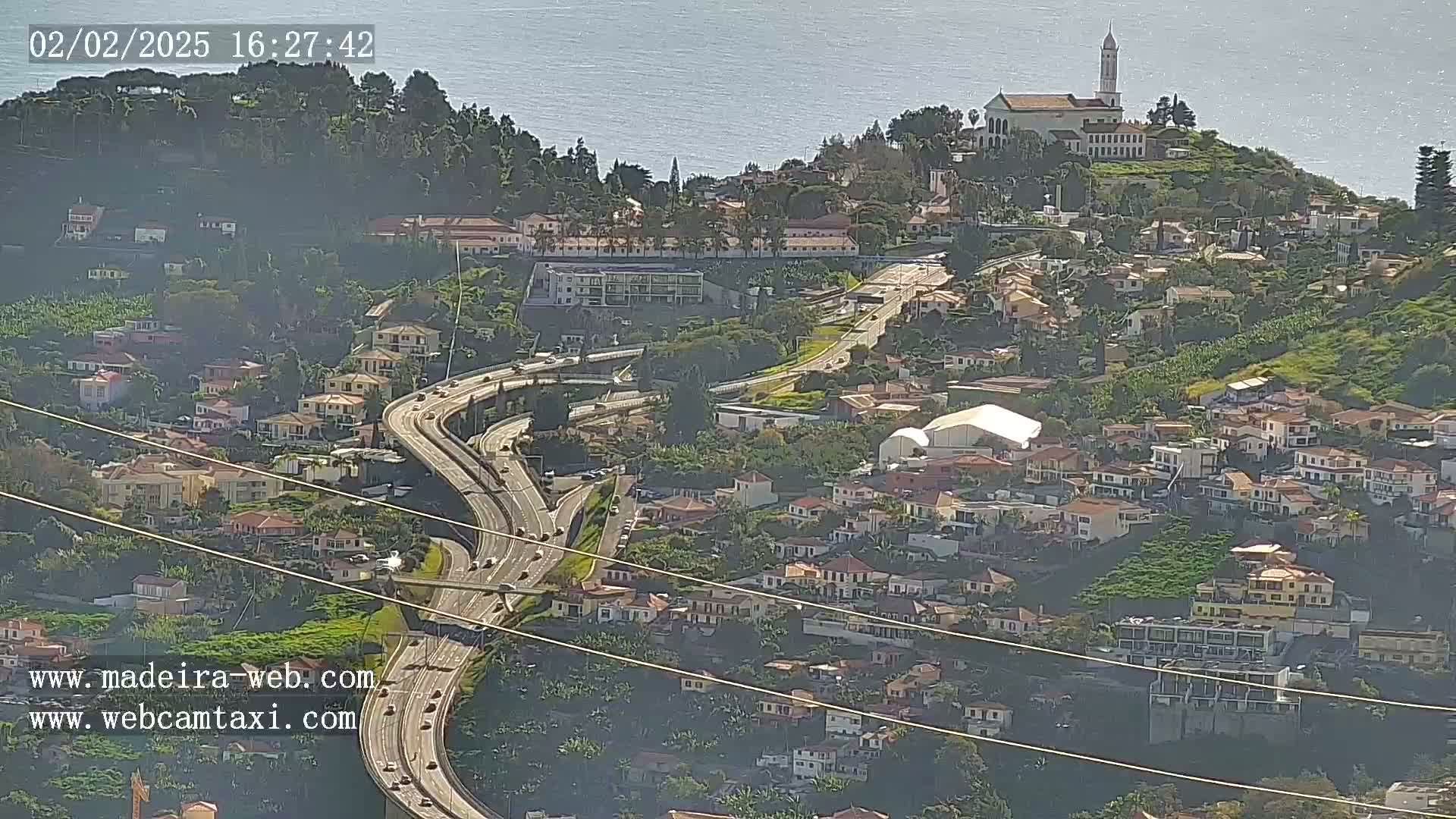 A hilly coastal town with a church atop a hill, a multi-lane highway weaving through it, and a clear, sunny day.