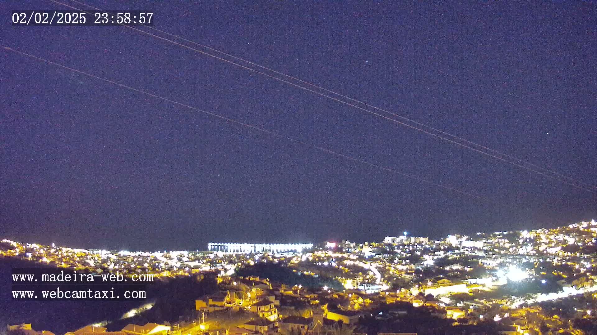 A nighttime view of a city illuminated by lights under a clear, dark sky with some faint stars visible.