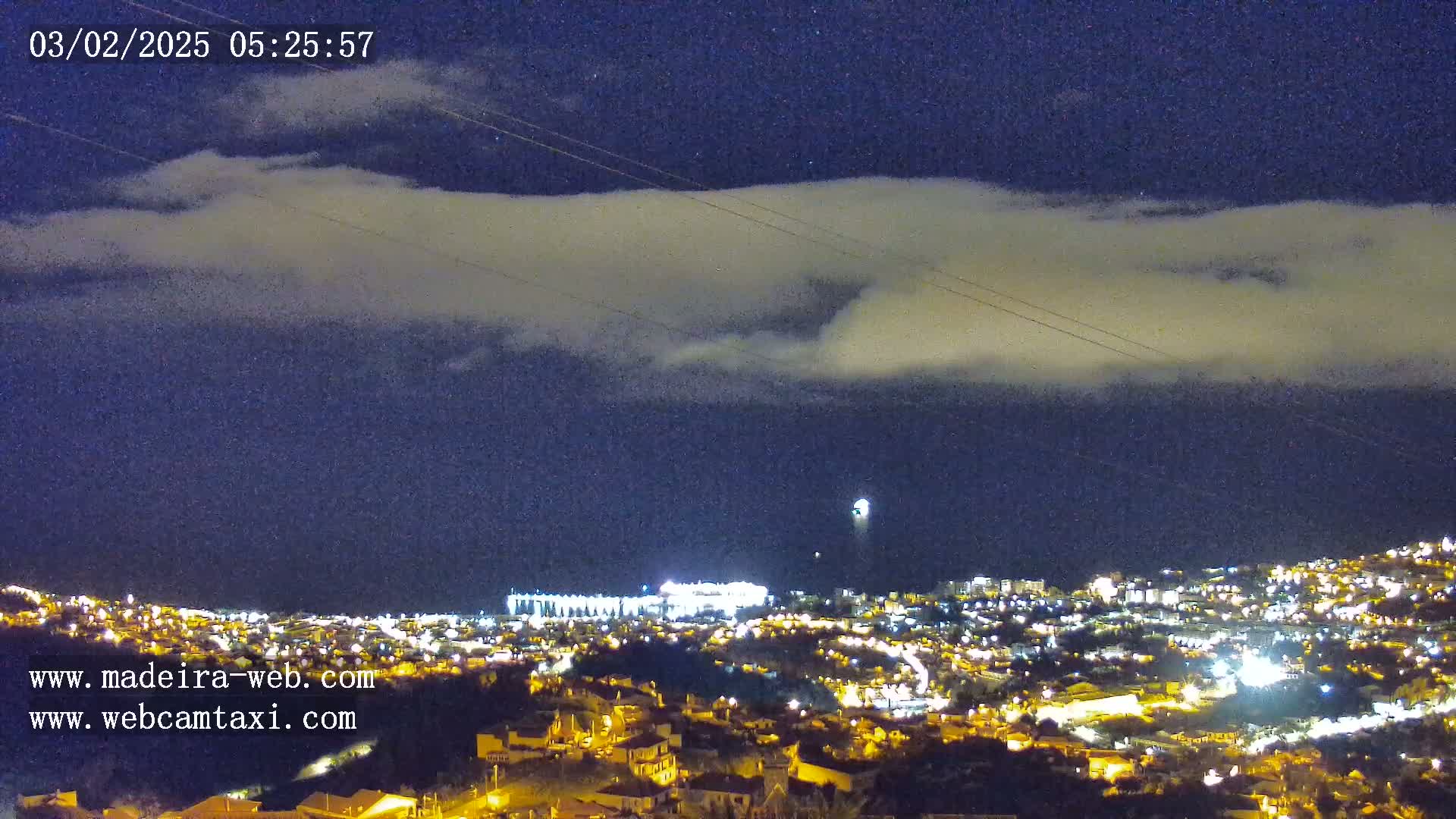 A nighttime view of a city illuminated by lights under a partly cloudy sky.