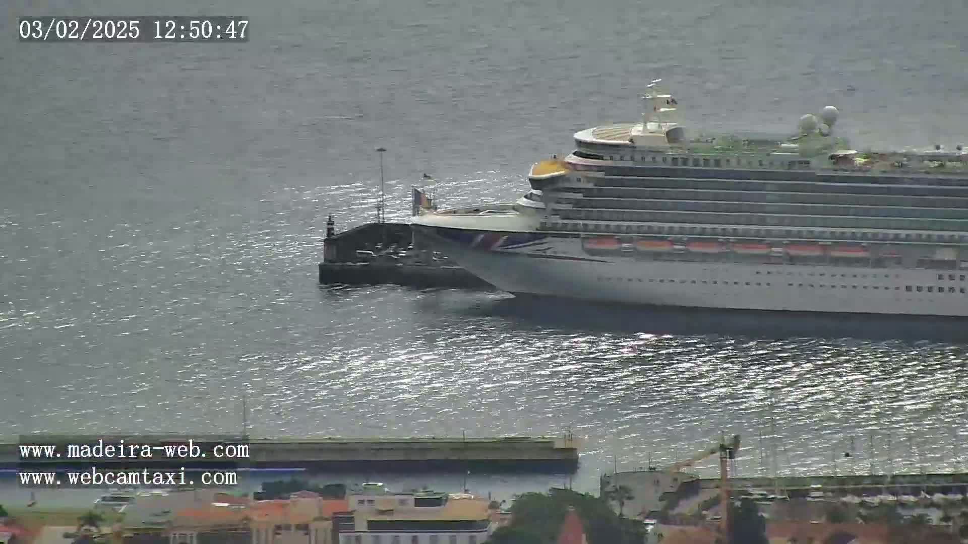 A large cruise ship is docked at a pier on a calm, sunny day.