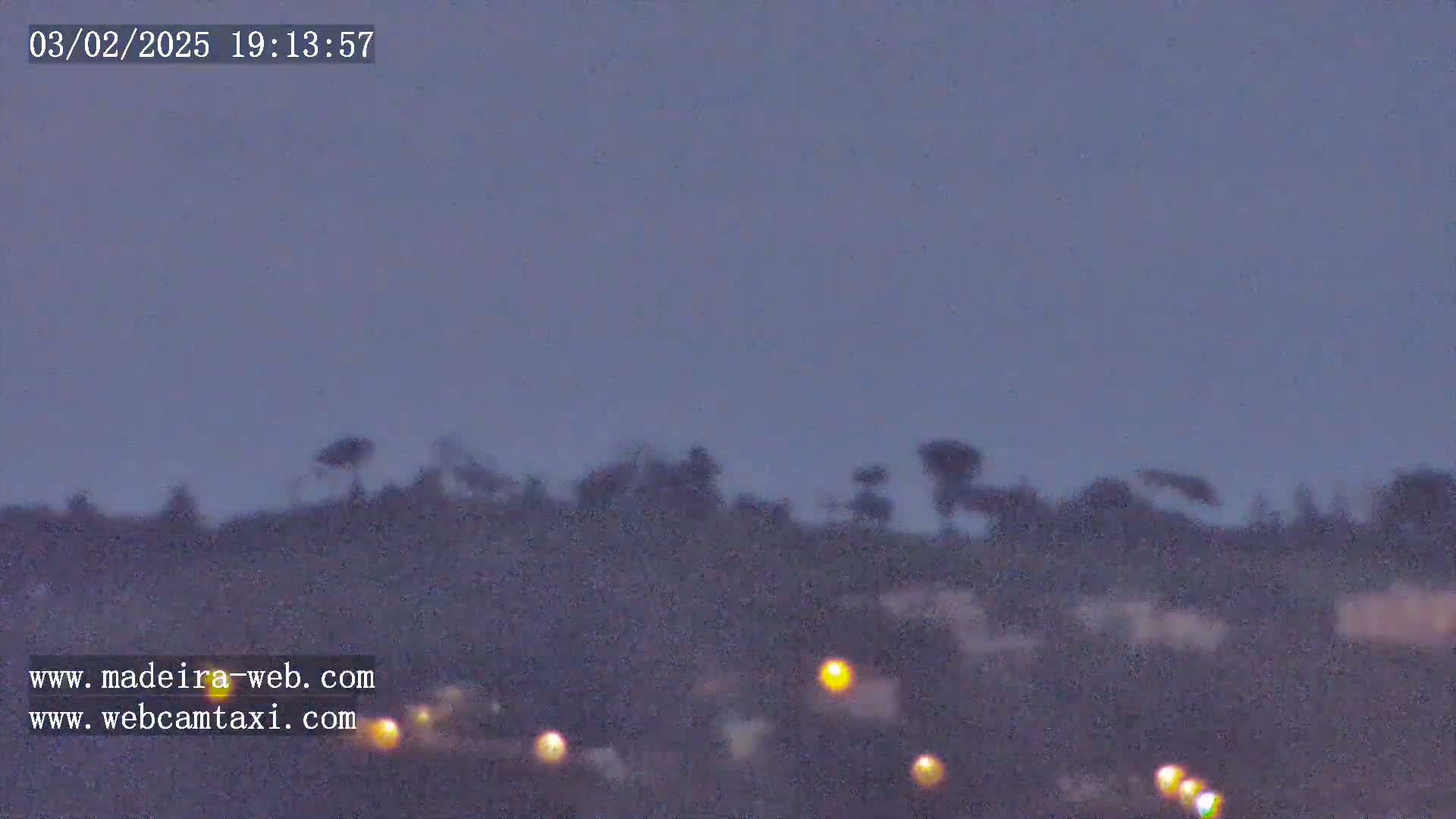 A blurry twilight view shows a dark hillside silhouetted against a dusky purple sky, with a few faint lights visible in the foreground.