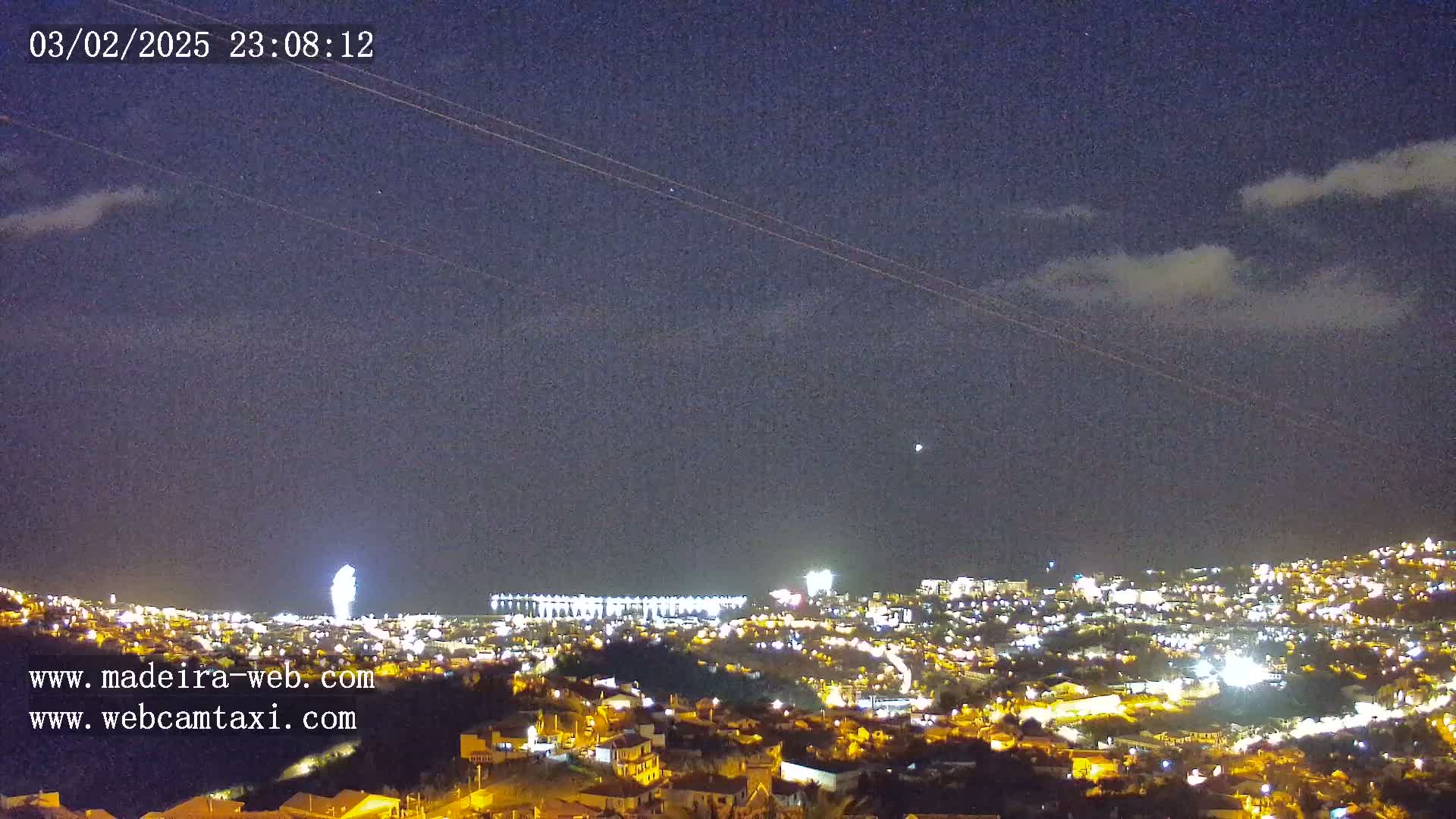 A nighttime view of a city illuminated with lights under a partly cloudy sky.