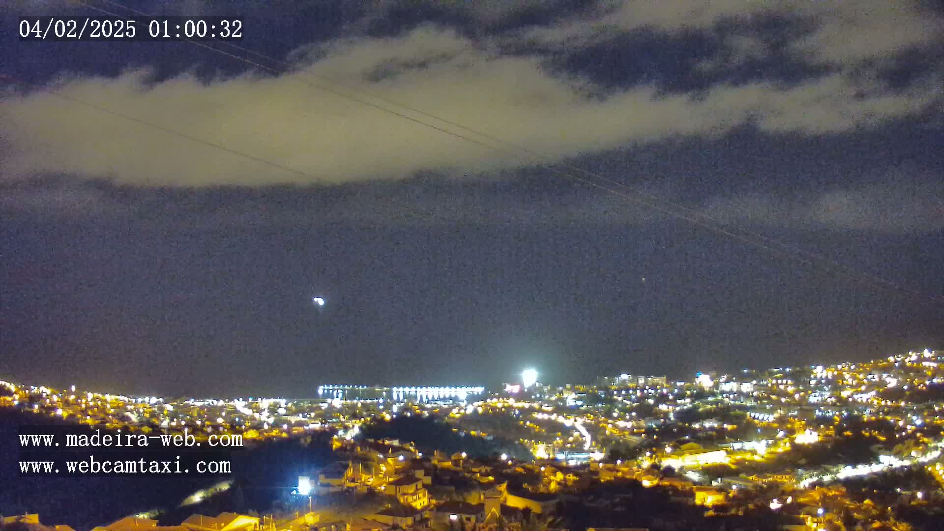 A nighttime view of a city illuminated by streetlights under a partly cloudy sky.
