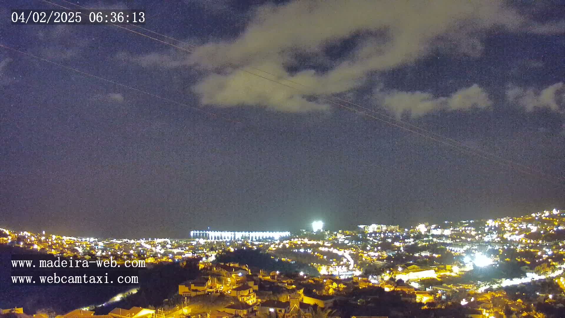 A nighttime view of a city illuminated with lights under a partly cloudy sky.