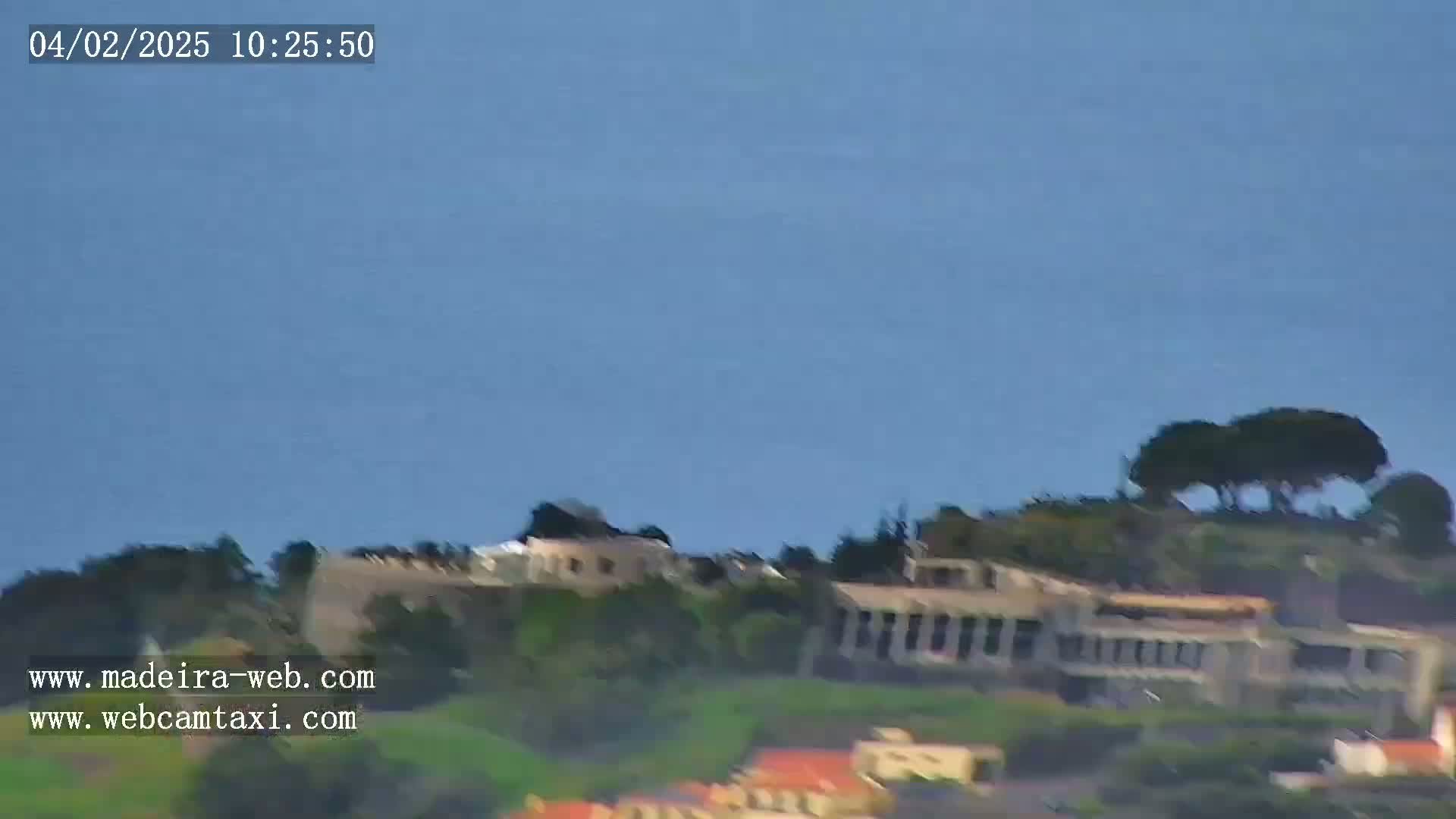 A distant view of buildings and trees on a hillside under a clear blue sky.