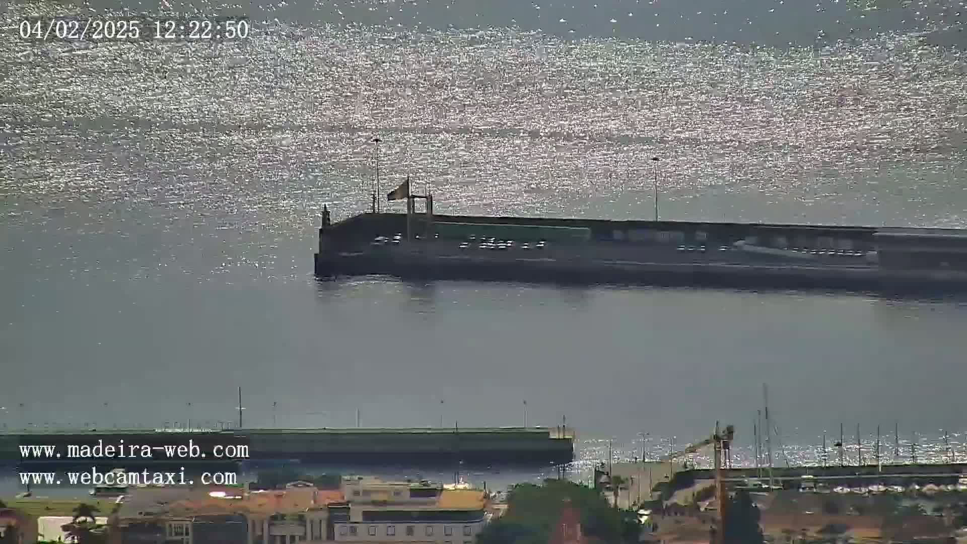 A long pier extends into a calm body of water shimmering under a bright, sunny sky.