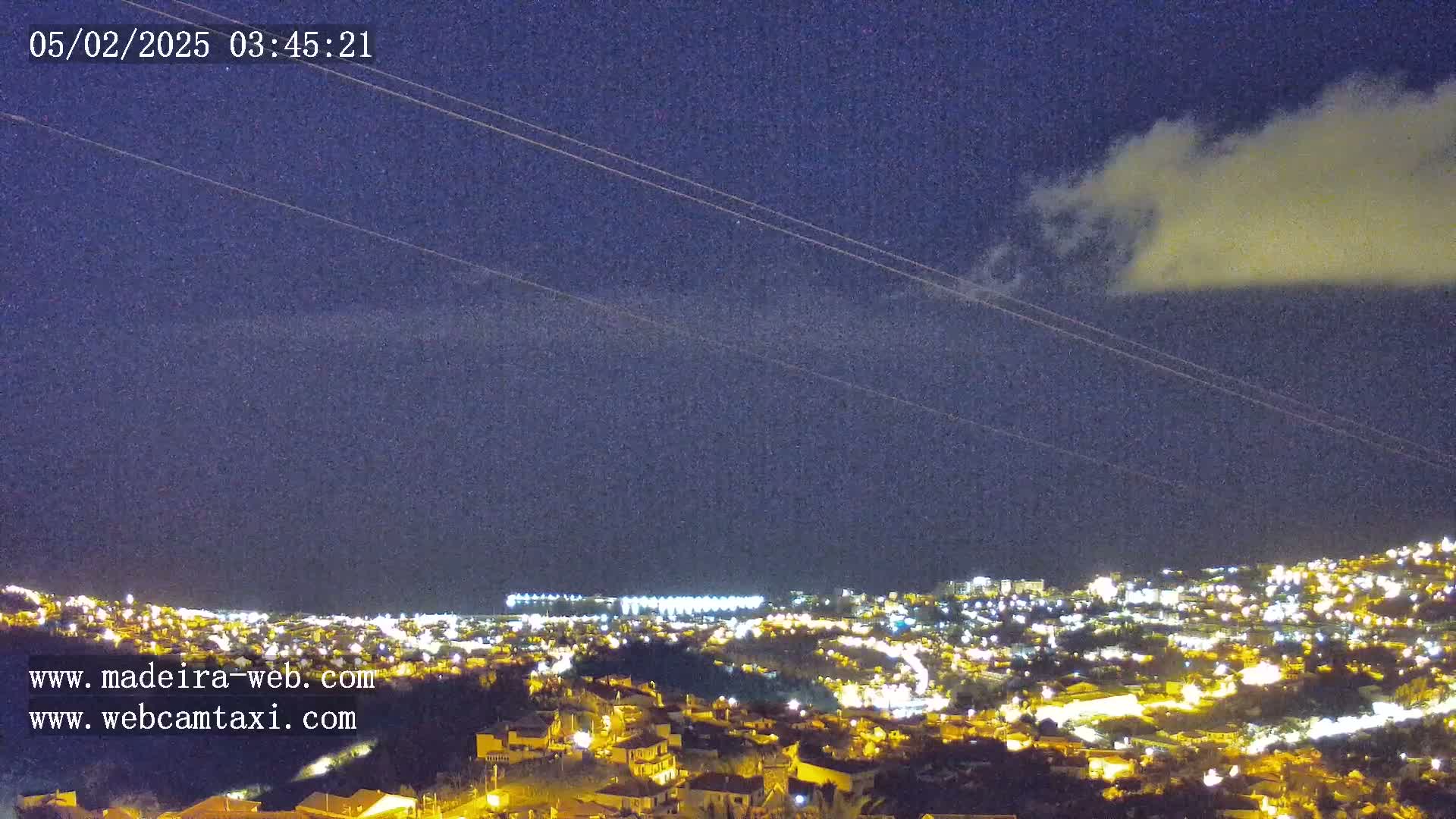 A nighttime view of a city illuminated by lights under a partly cloudy sky.