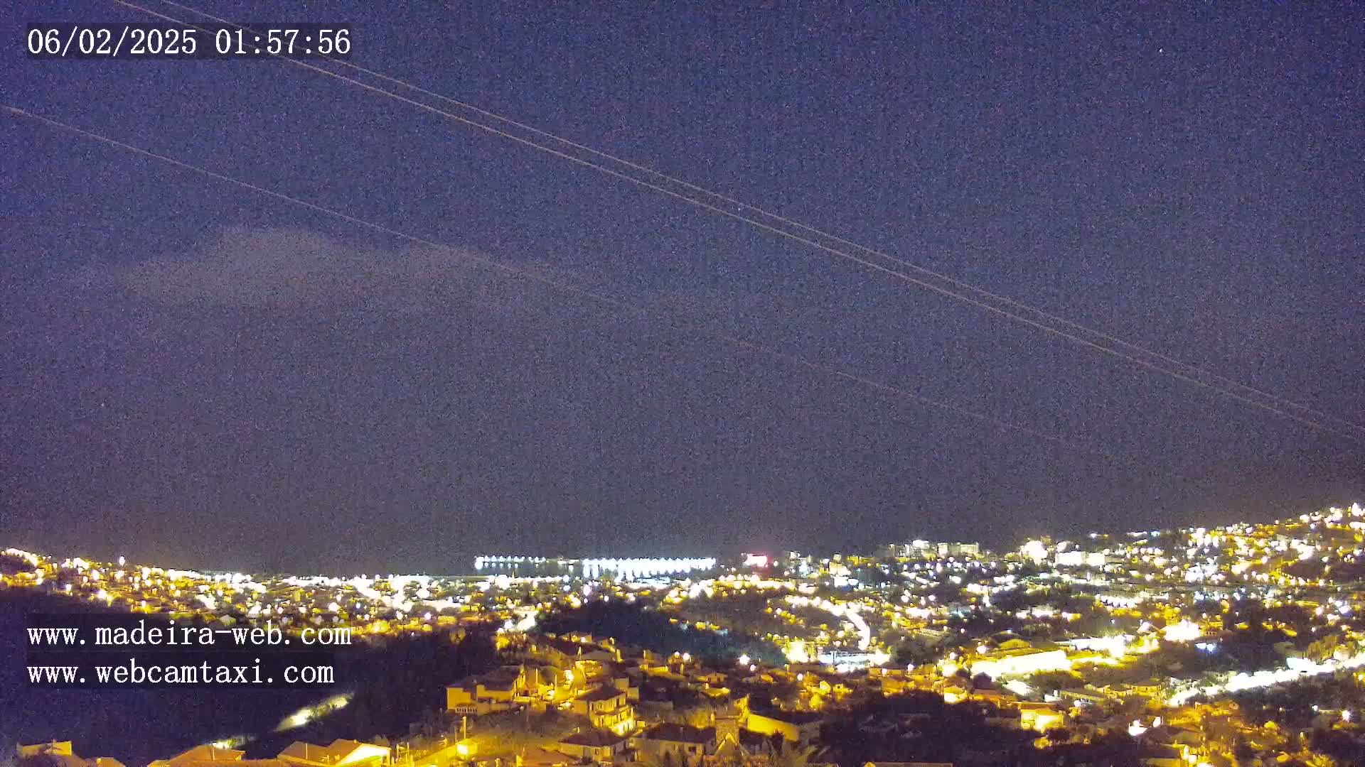 A nighttime view of a city illuminated by lights, situated on a hillside under a mostly clear, dark sky.