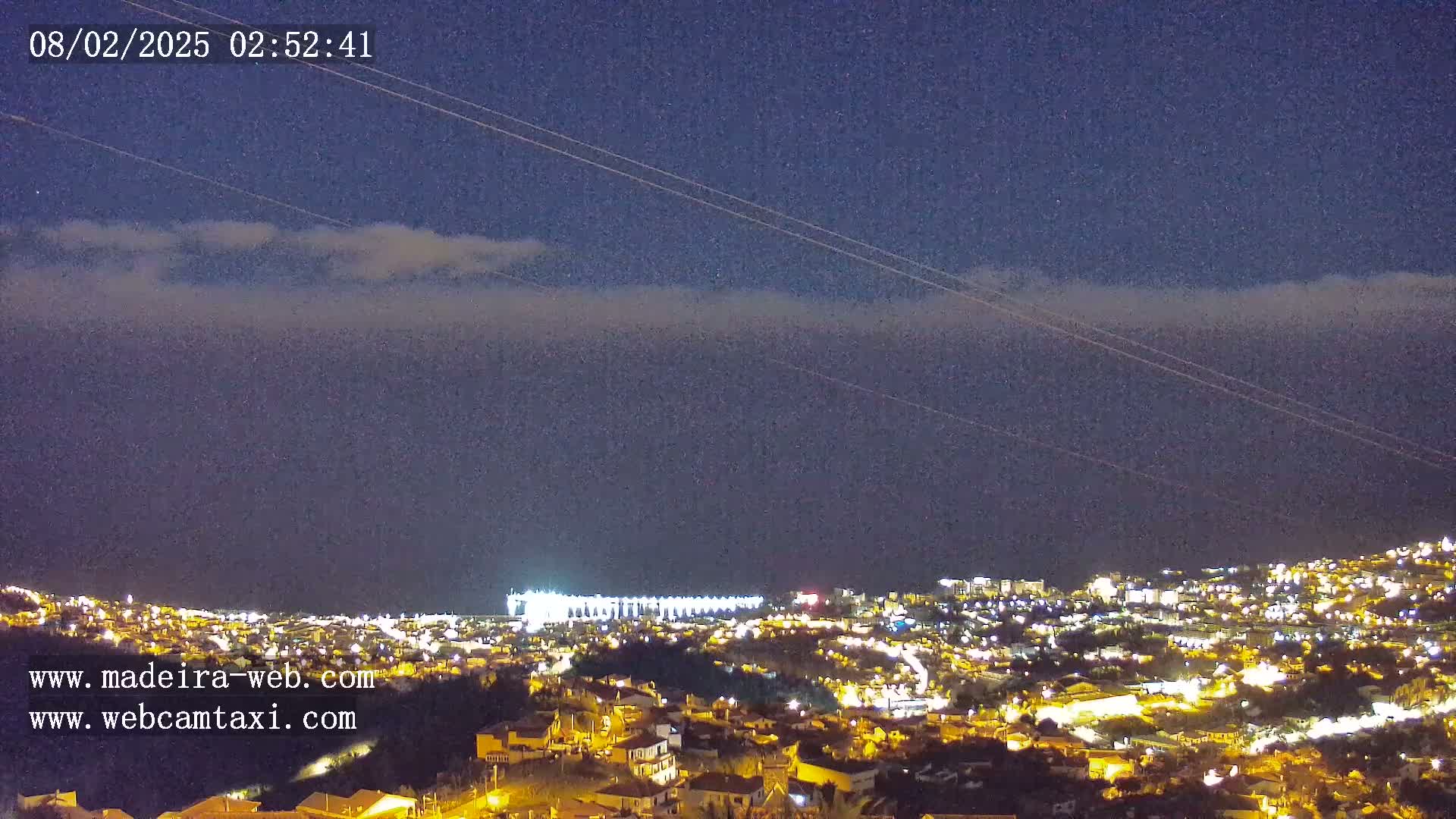 A nighttime view of a city illuminated by lights, under a slightly cloudy sky.