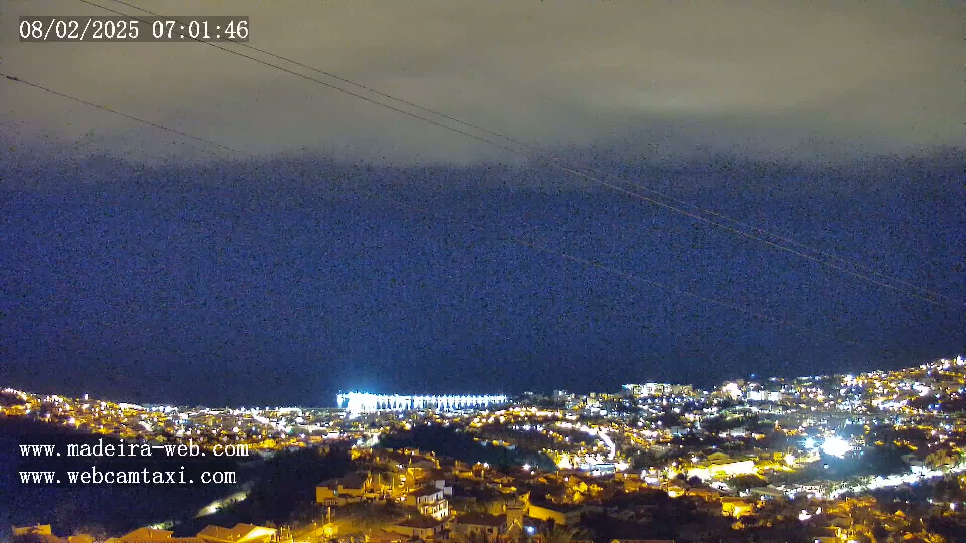 A nighttime view of a city illuminated by lights, under a dark, cloudy sky.