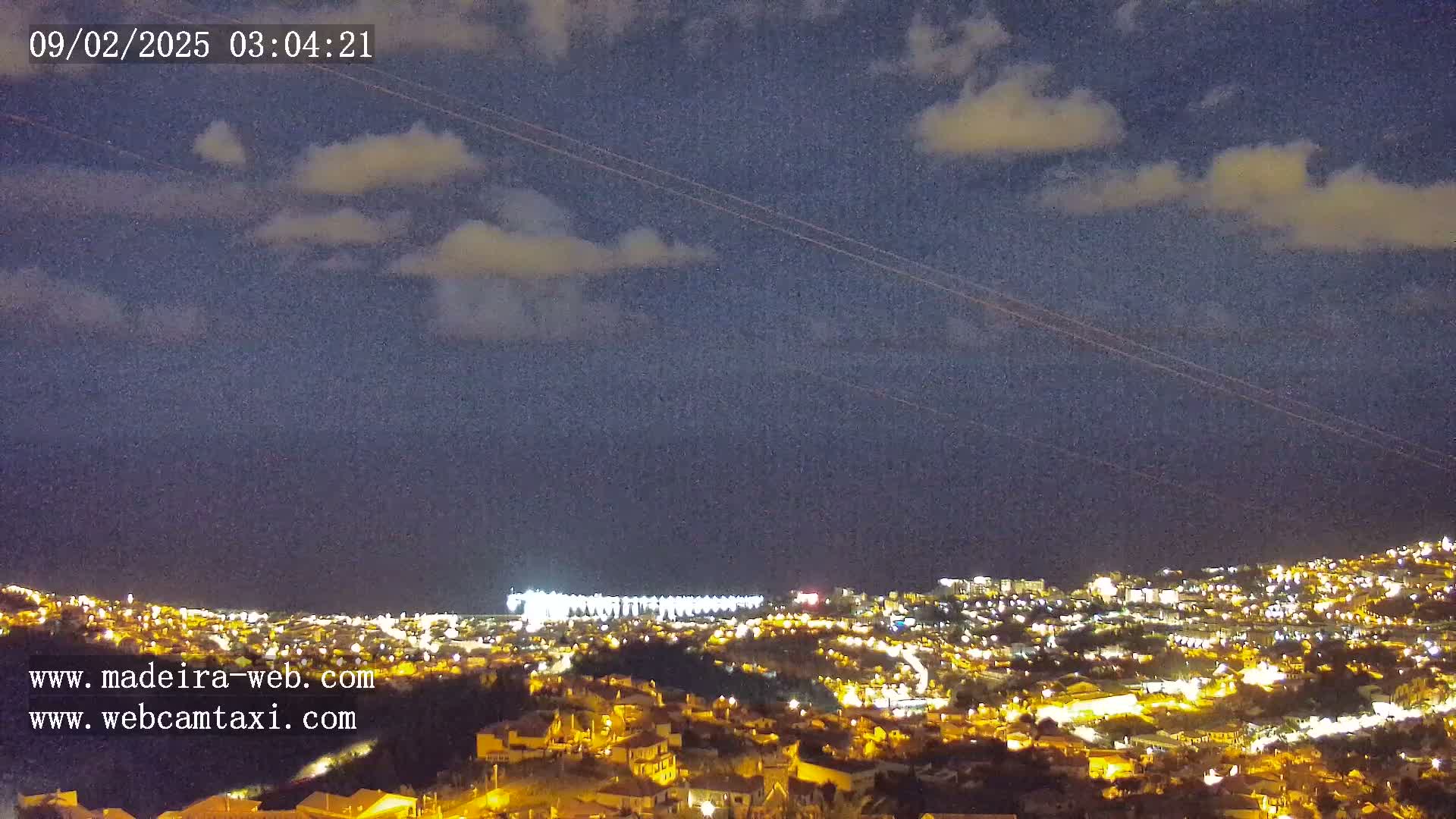 A nighttime view of a city illuminated by lights, under a partly cloudy sky.