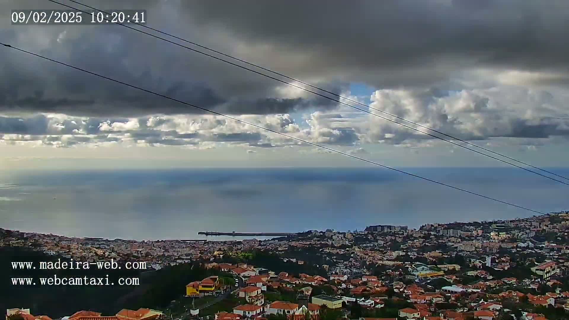 A coastal city sprawls beneath a partly cloudy sky, overlooking a calm ocean.