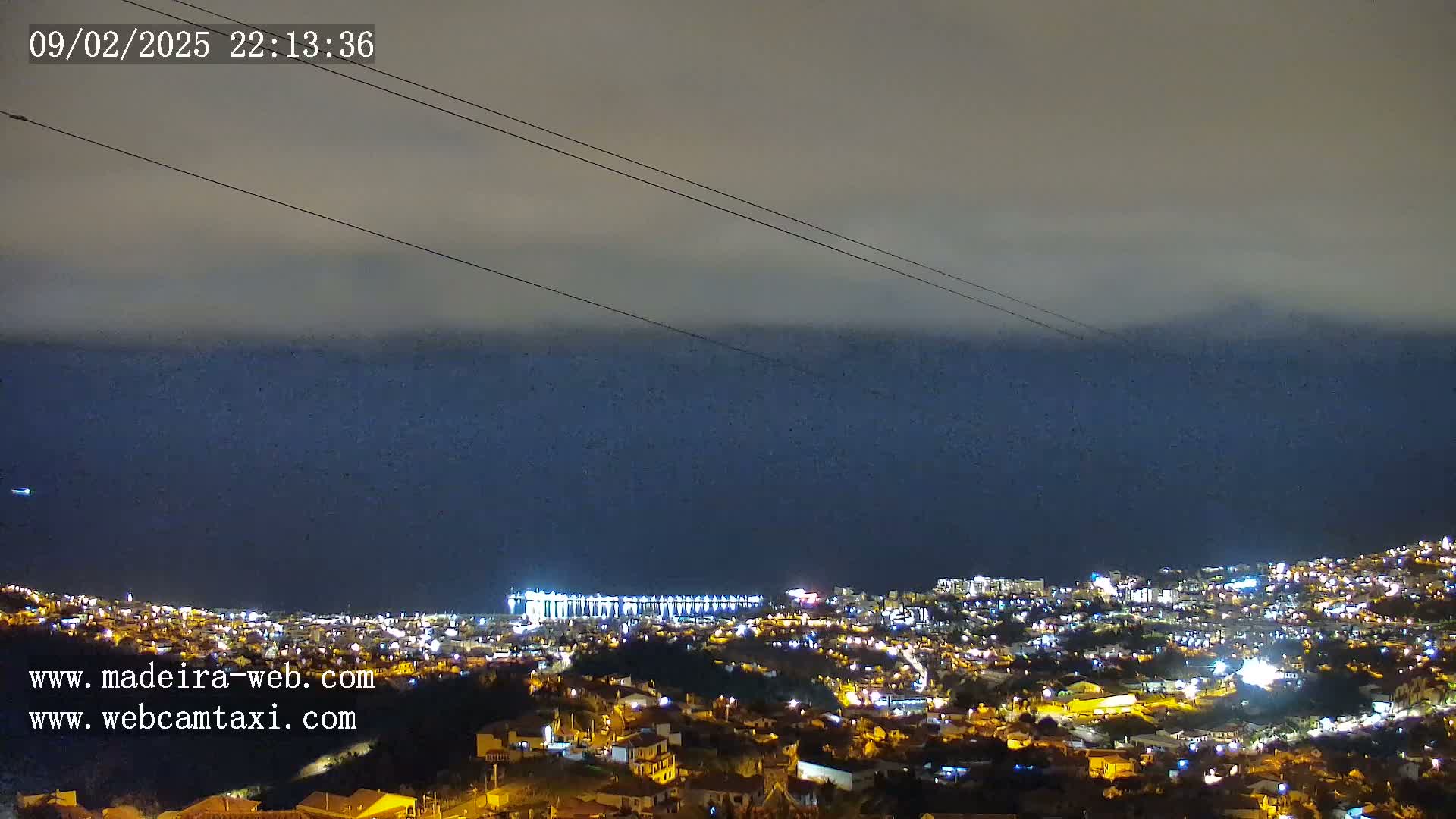 A nighttime view of a coastal city illuminated with lights under a cloudy sky.