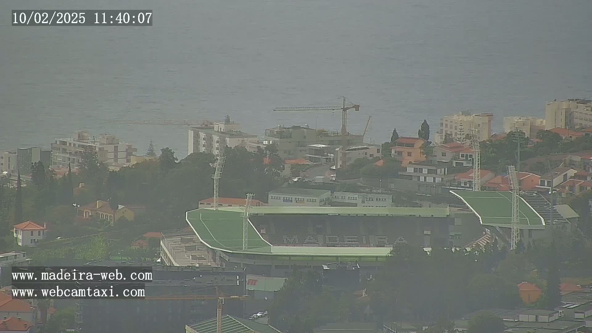 A hazy view shows a soccer stadium nestled among buildings near a coastline.