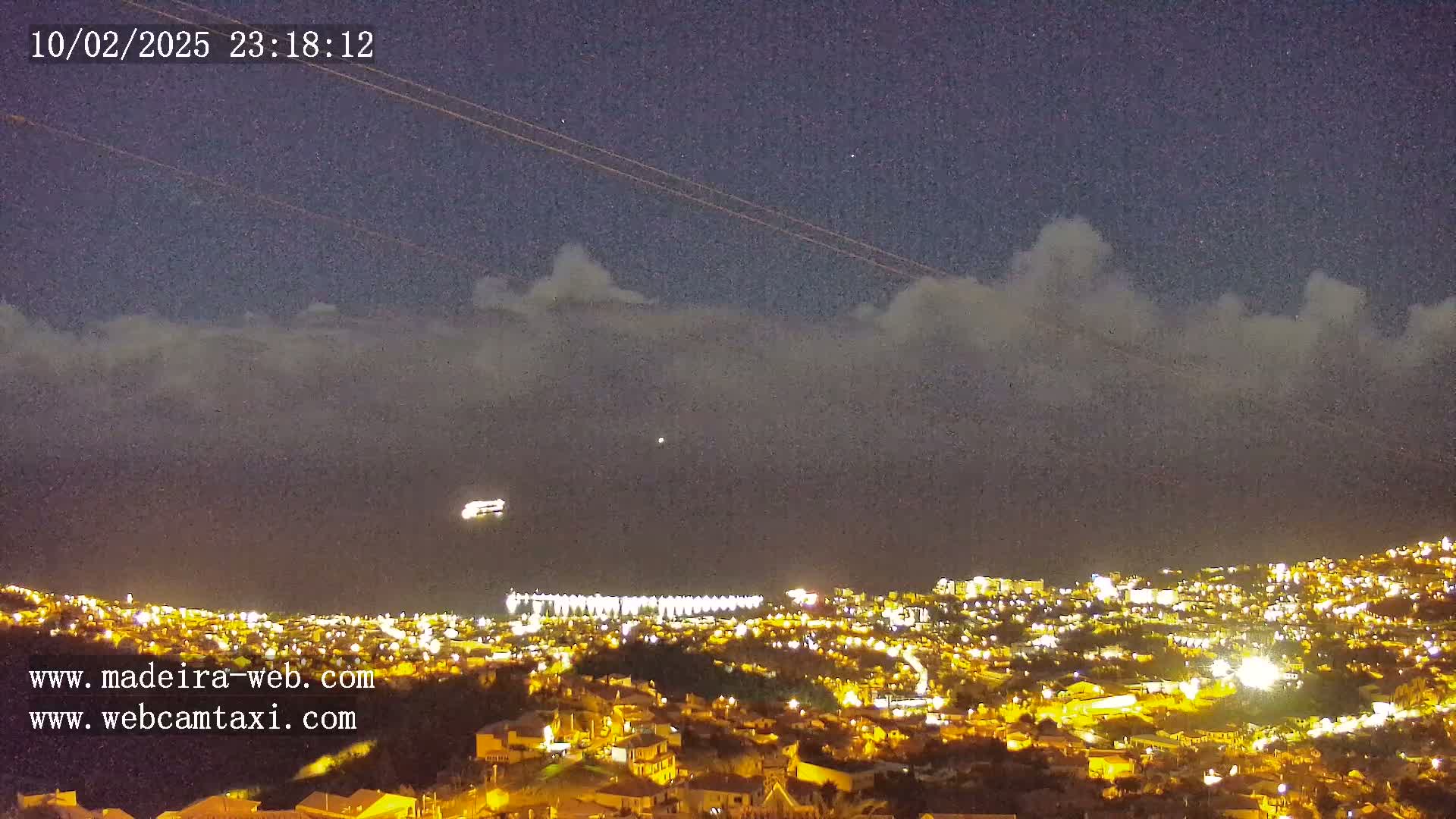 A nighttime view of a city illuminated by lights under a partly cloudy sky.