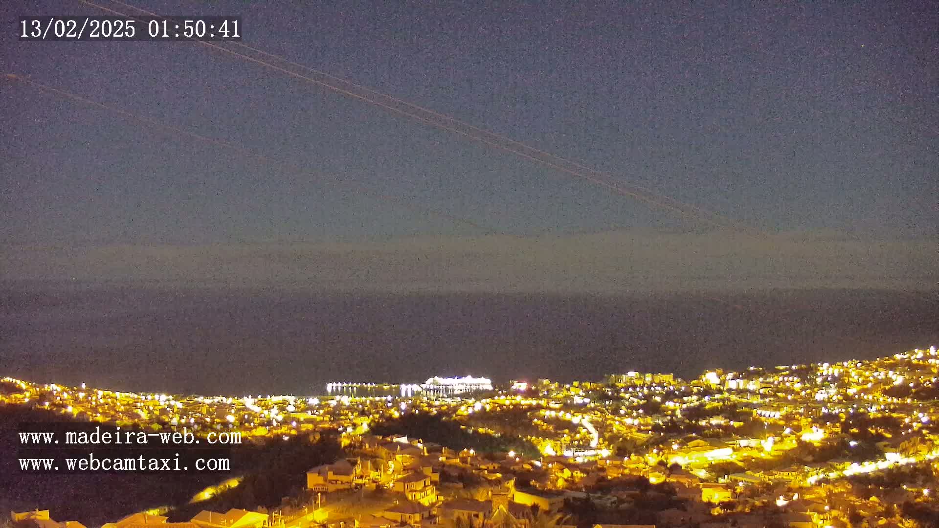 A nighttime, long shot of a coastal city illuminated with lights, under a clear, dark sky.