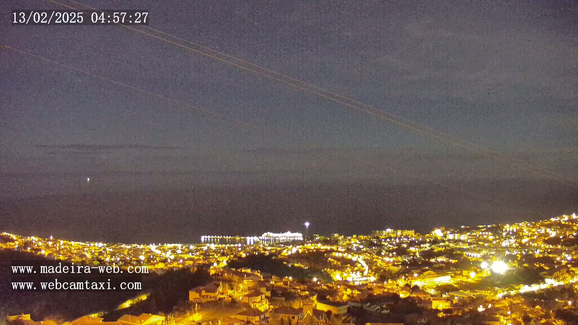 A nighttime, long-range view of a city illuminated by lights, situated on a hillside overlooking a dark ocean under a clear, dark sky.