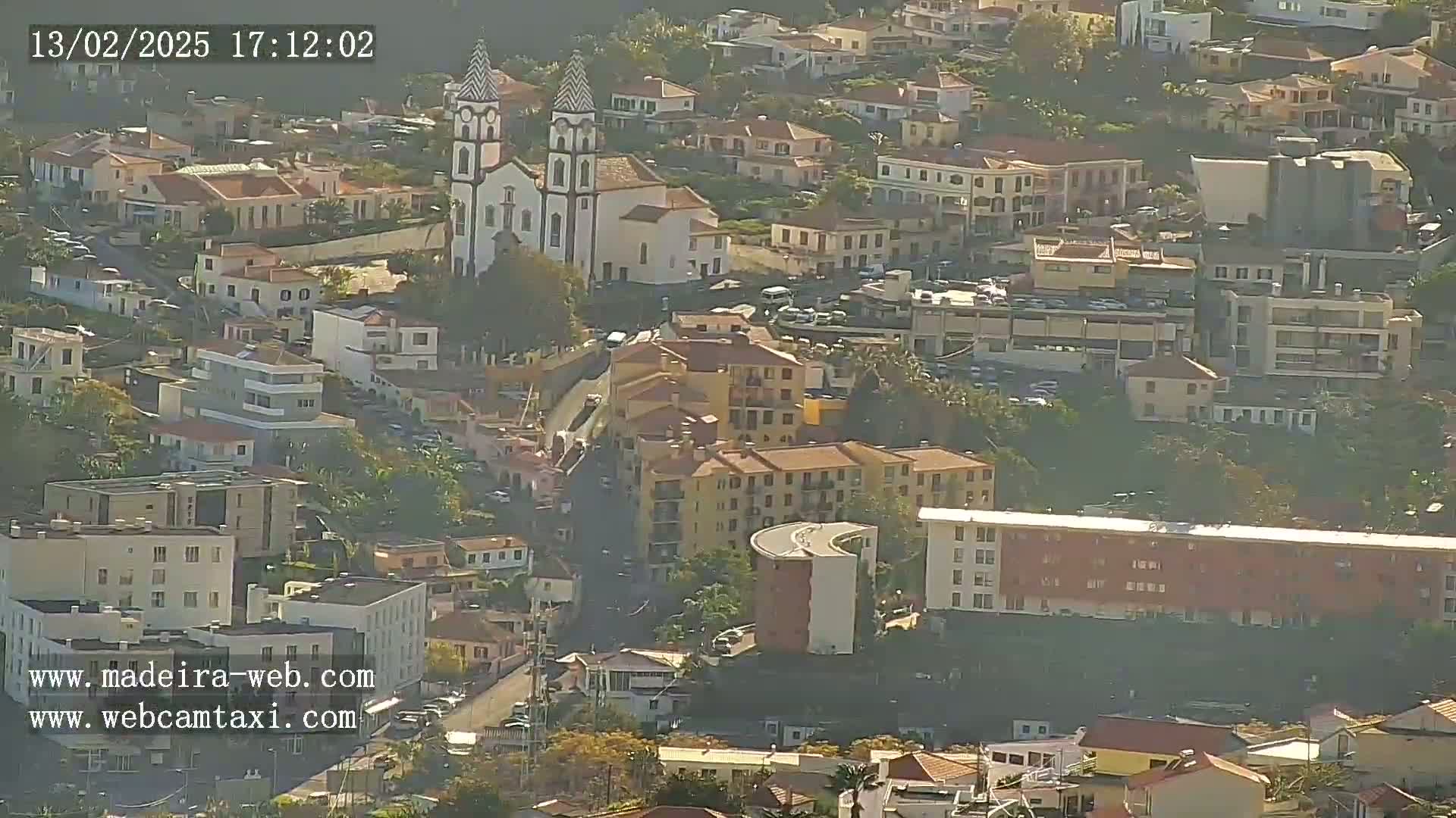 An aerial view shows a town with a white church and numerous buildings, under sunny and hazy conditions.