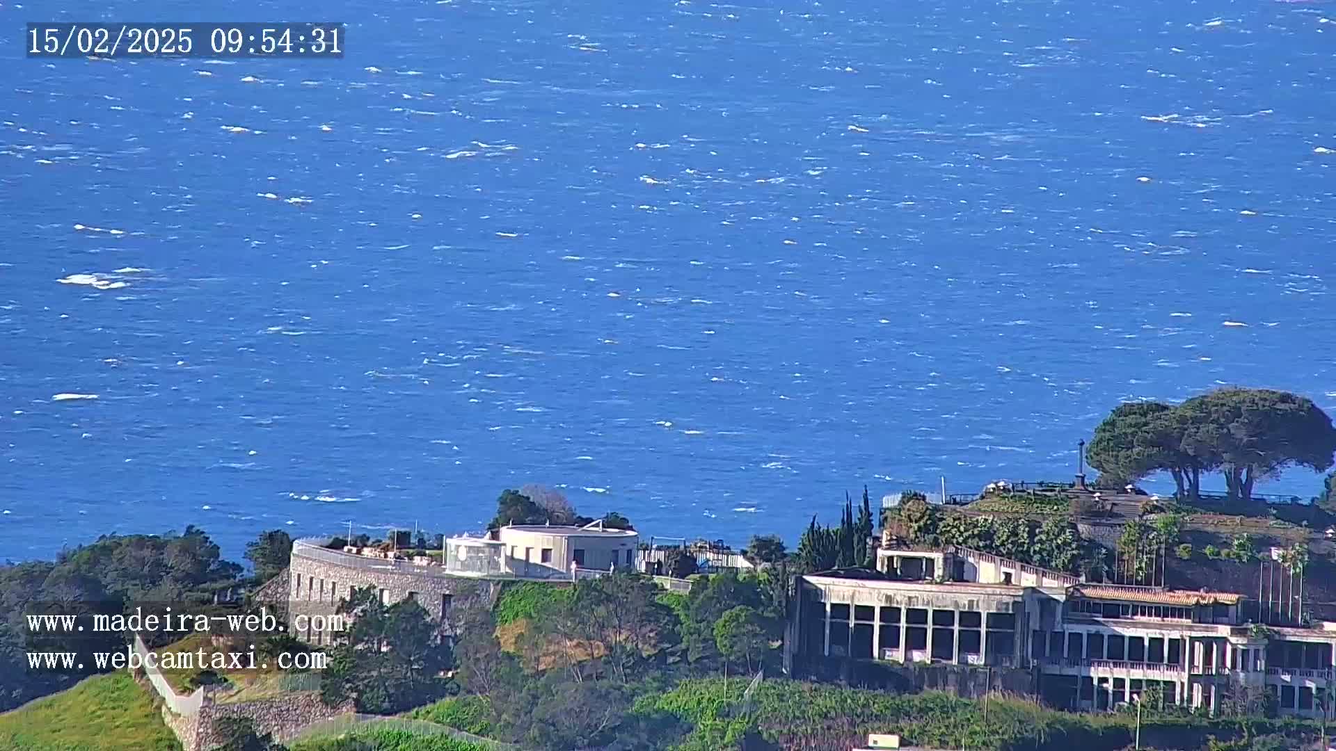 A windy day shows a large building complex overlooking a blue, choppy ocean.