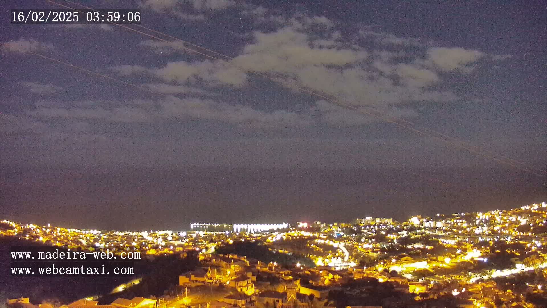 A nighttime view of a city illuminated by lights under a partly cloudy sky.