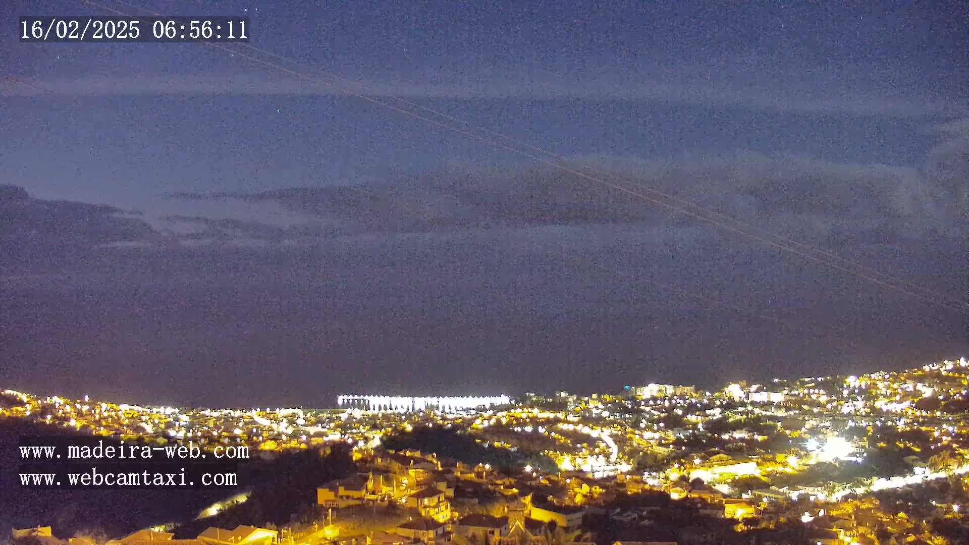 A nighttime view of a city illuminated with lights, partially obscured by a layer of clouds under a dark sky.