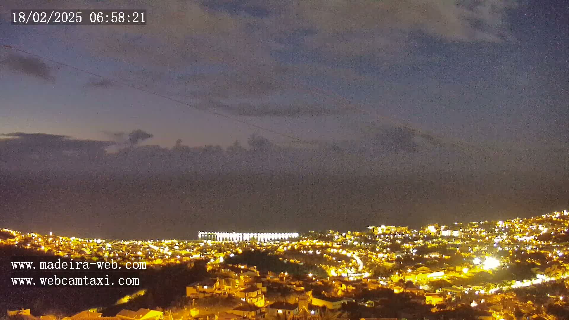 A nighttime view of a city illuminated by lights, under a mostly cloudy sky.