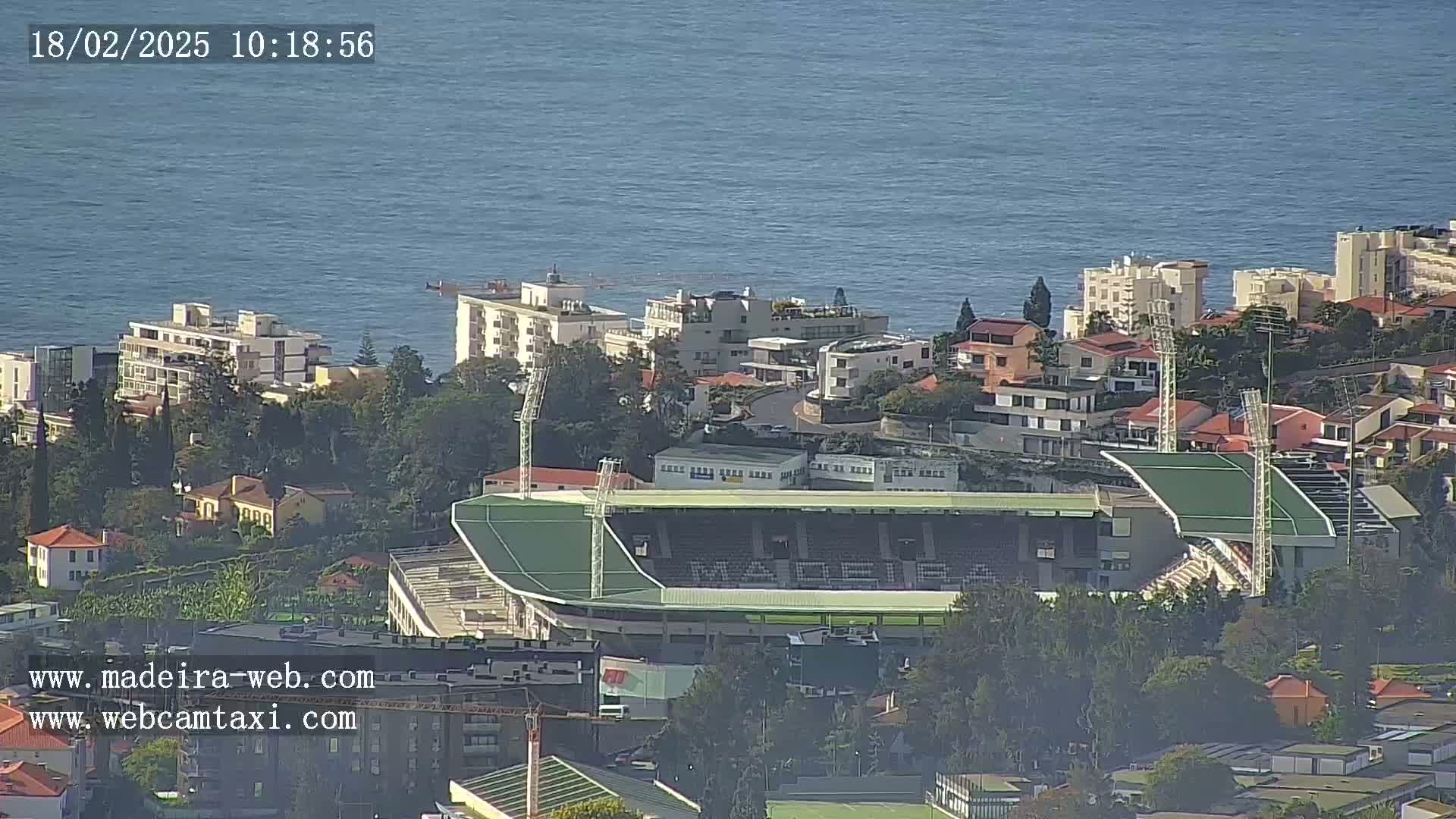 A coastal town with a green stadium is seen on a hazy day, overlooking a calm ocean.