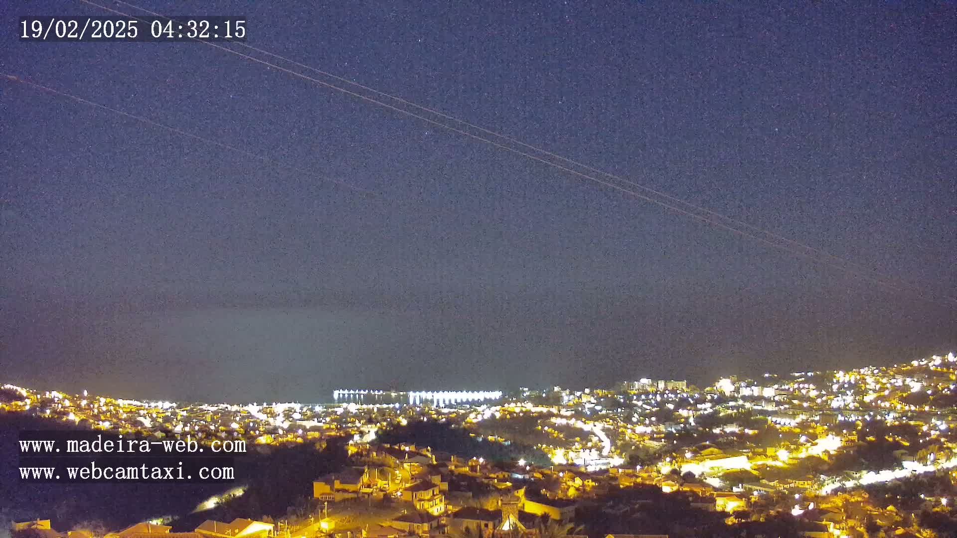 A nighttime, high-angle view shows a city illuminated by lights against a dark, clear sky dotted with stars.