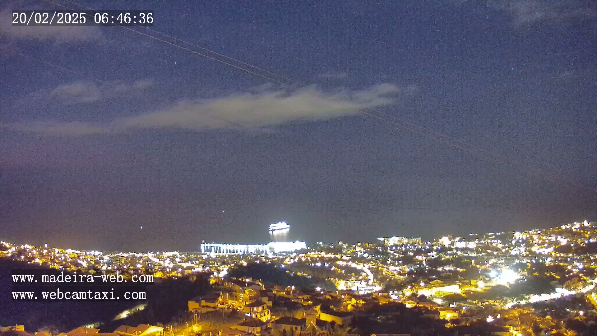 A nighttime view of a city illuminated by lights under a mostly clear sky with a thin layer of clouds.