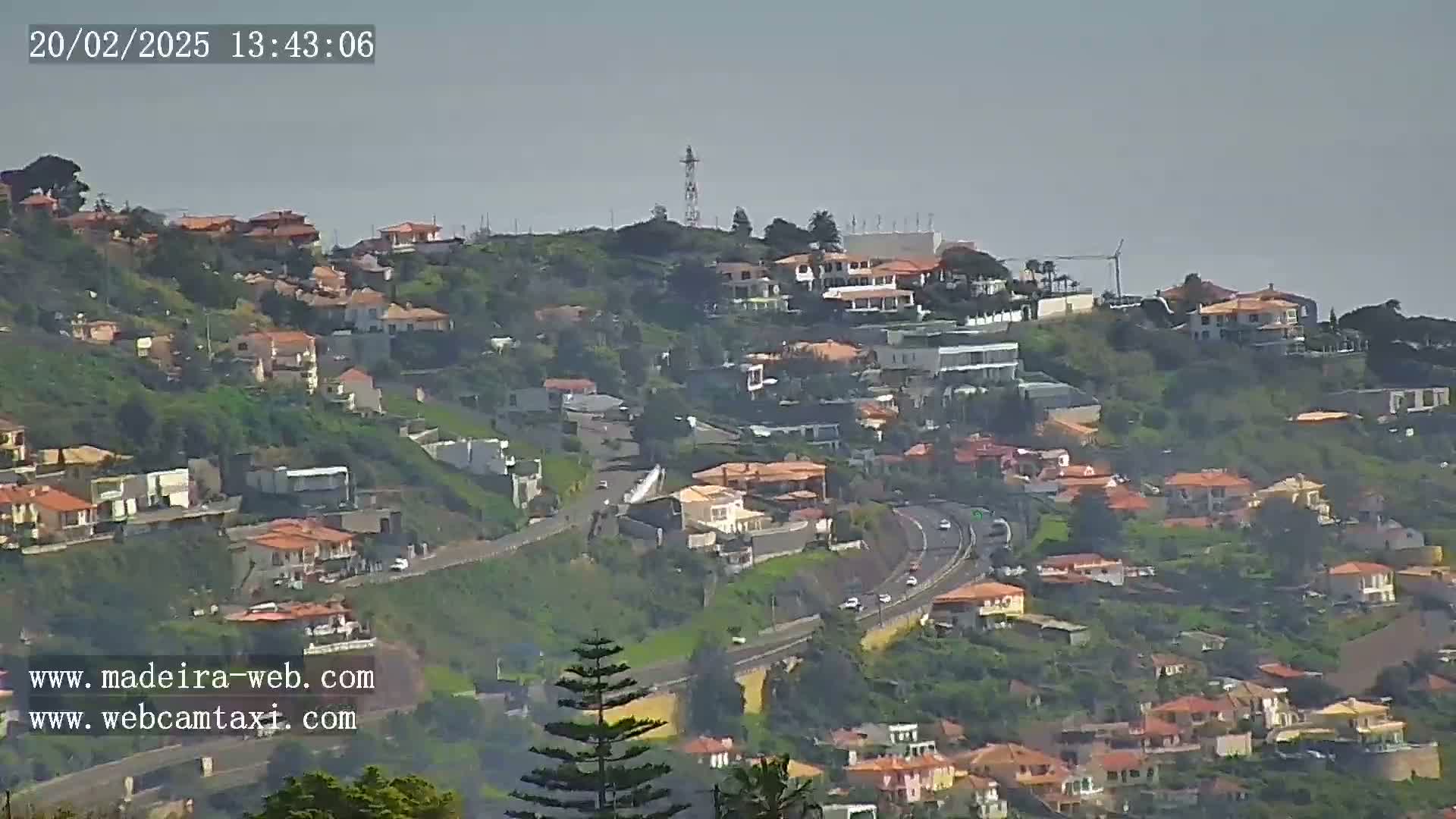 A hazy view shows a hillside covered in houses and vegetation, with a highway winding through it.