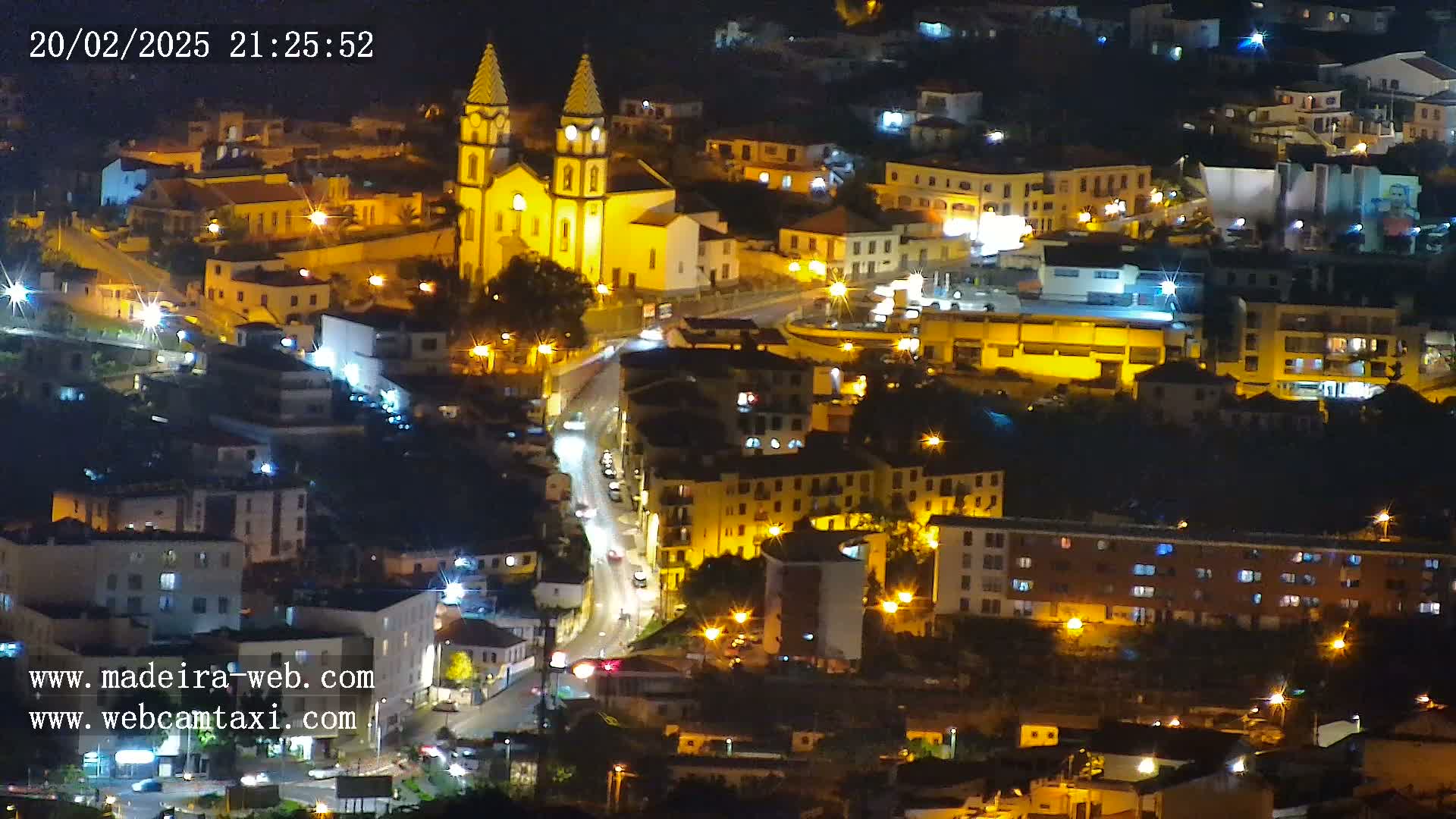 A nighttime aerial view of a town illuminated by streetlights, centered on a large, brightly lit church.