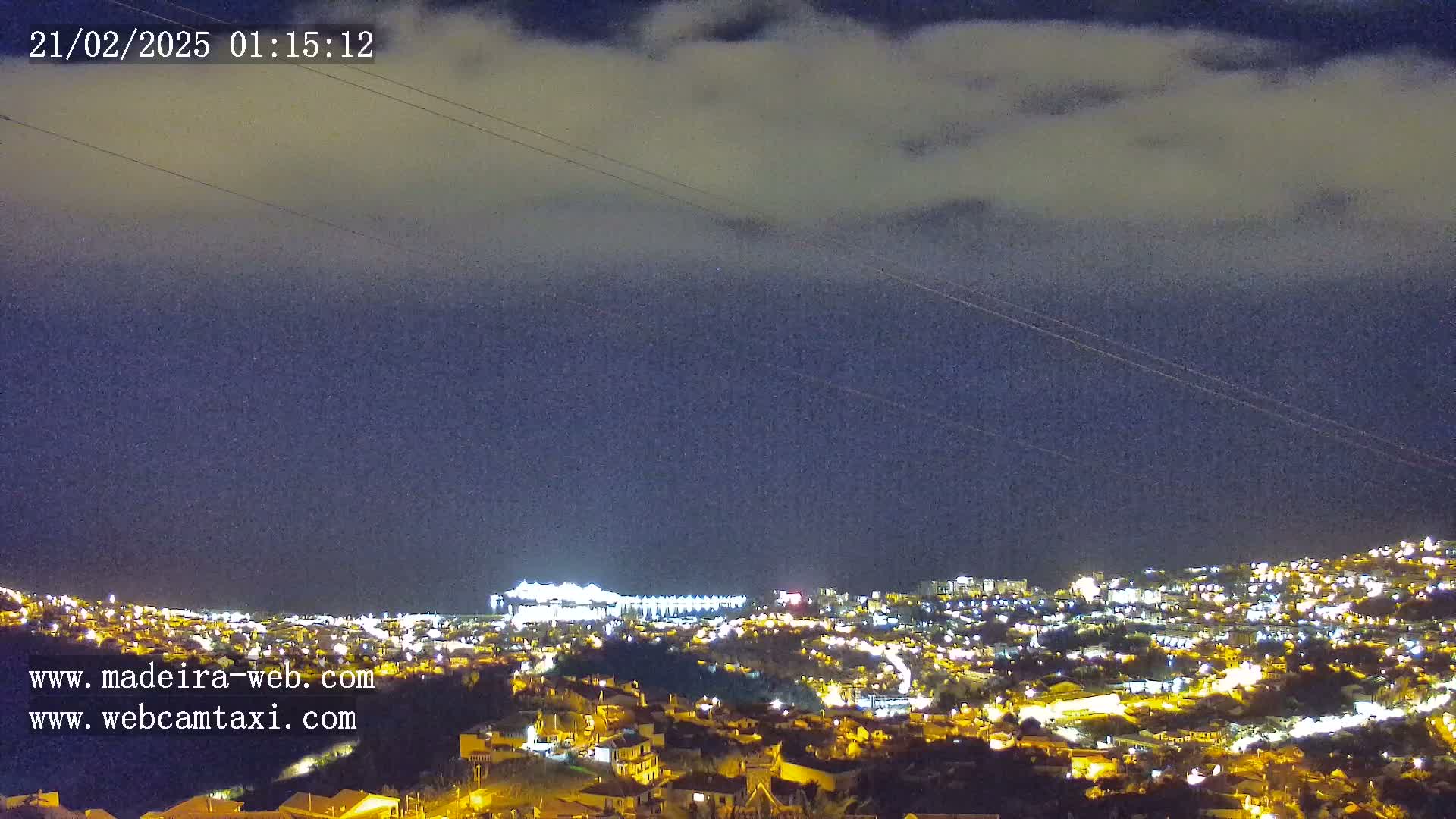 A nighttime view of a city illuminated by streetlights under a partly cloudy sky.