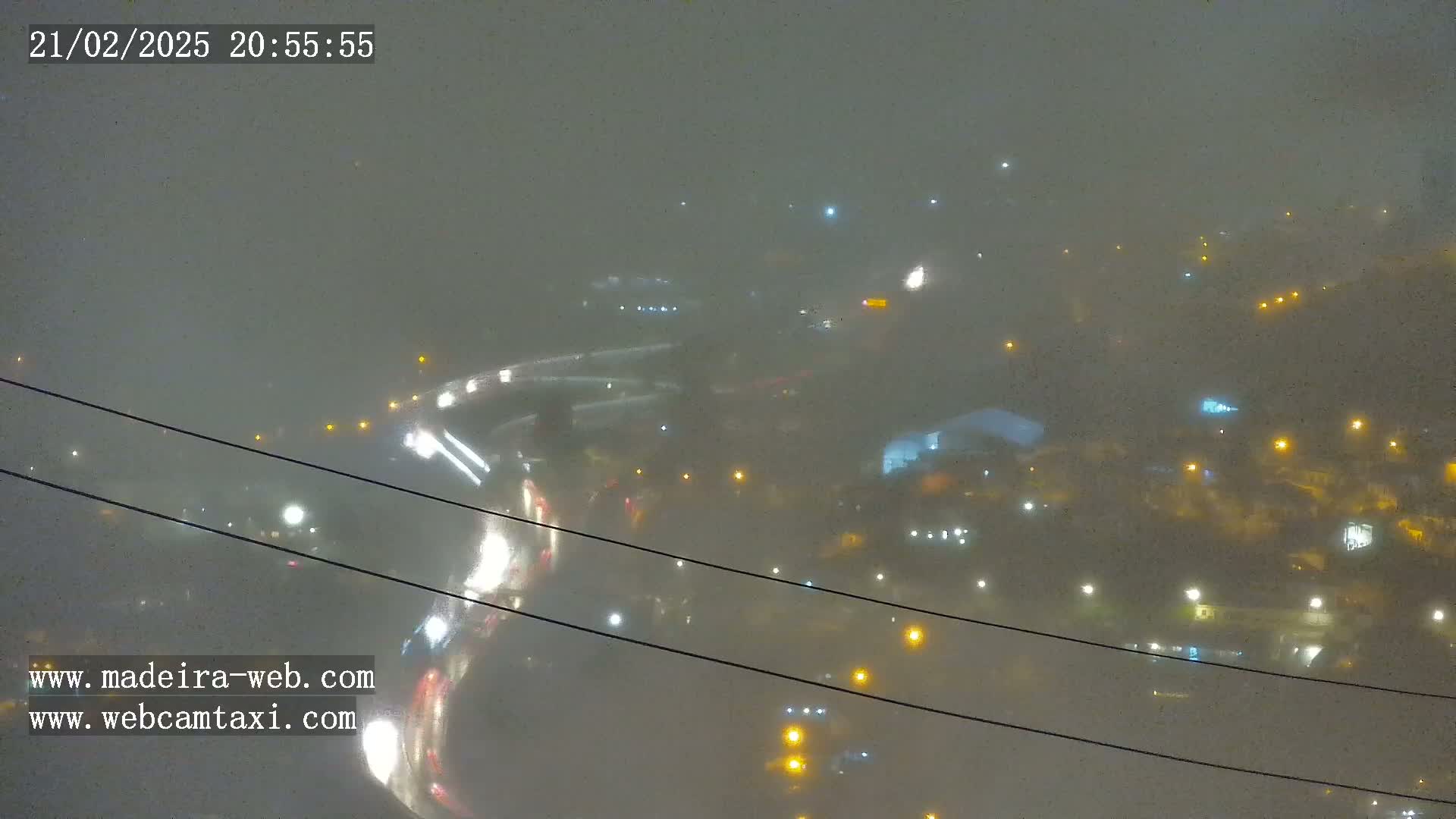 A nighttime, foggy view of a hilly town with scattered streetlights and roadways, seen from an elevated perspective.