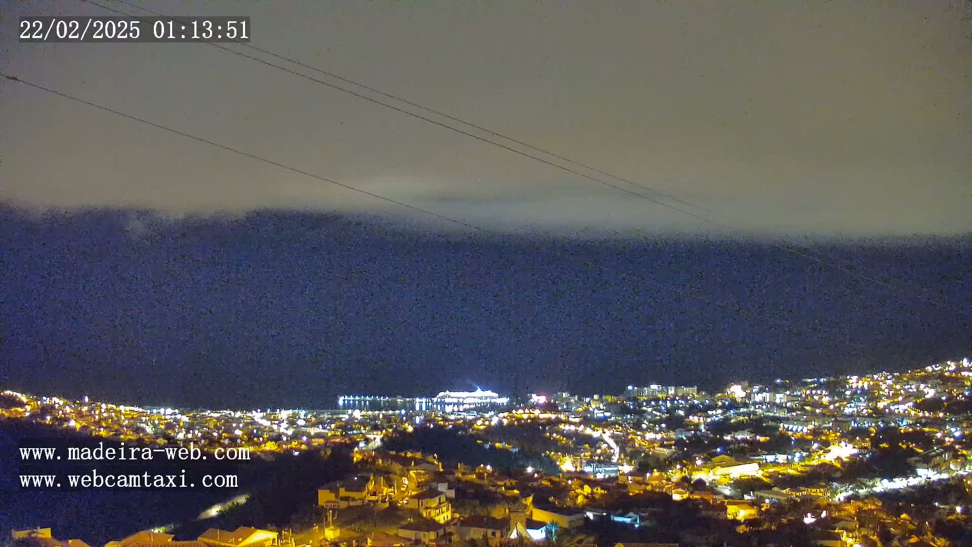 A nighttime view of a city illuminated by lights, with a layer of clouds or fog obscuring the sky.