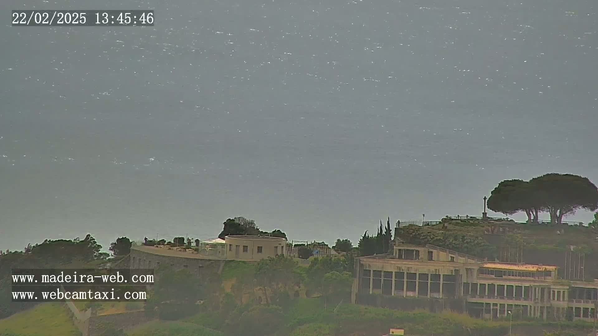 A hazy view of a calm ocean with buildings and trees on a hillside in the foreground.
