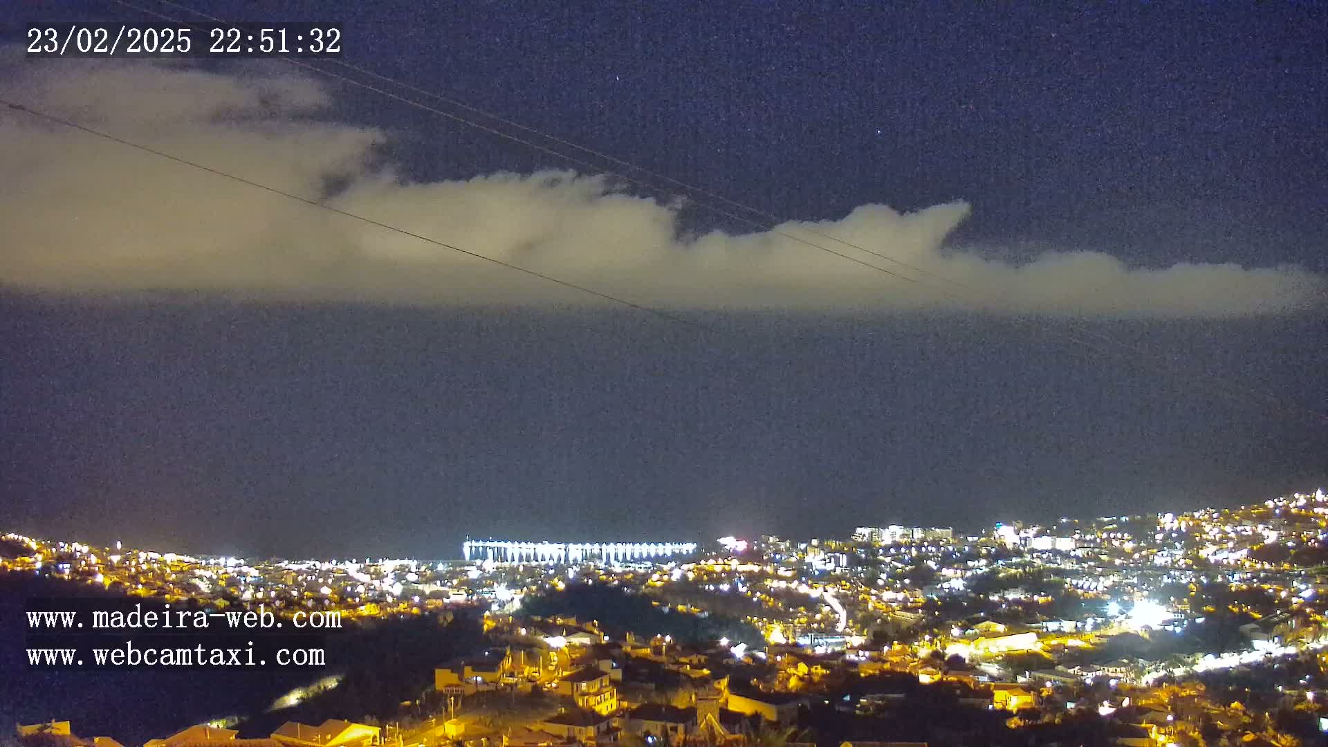 A nighttime view of a city illuminated with lights under a partly cloudy sky.