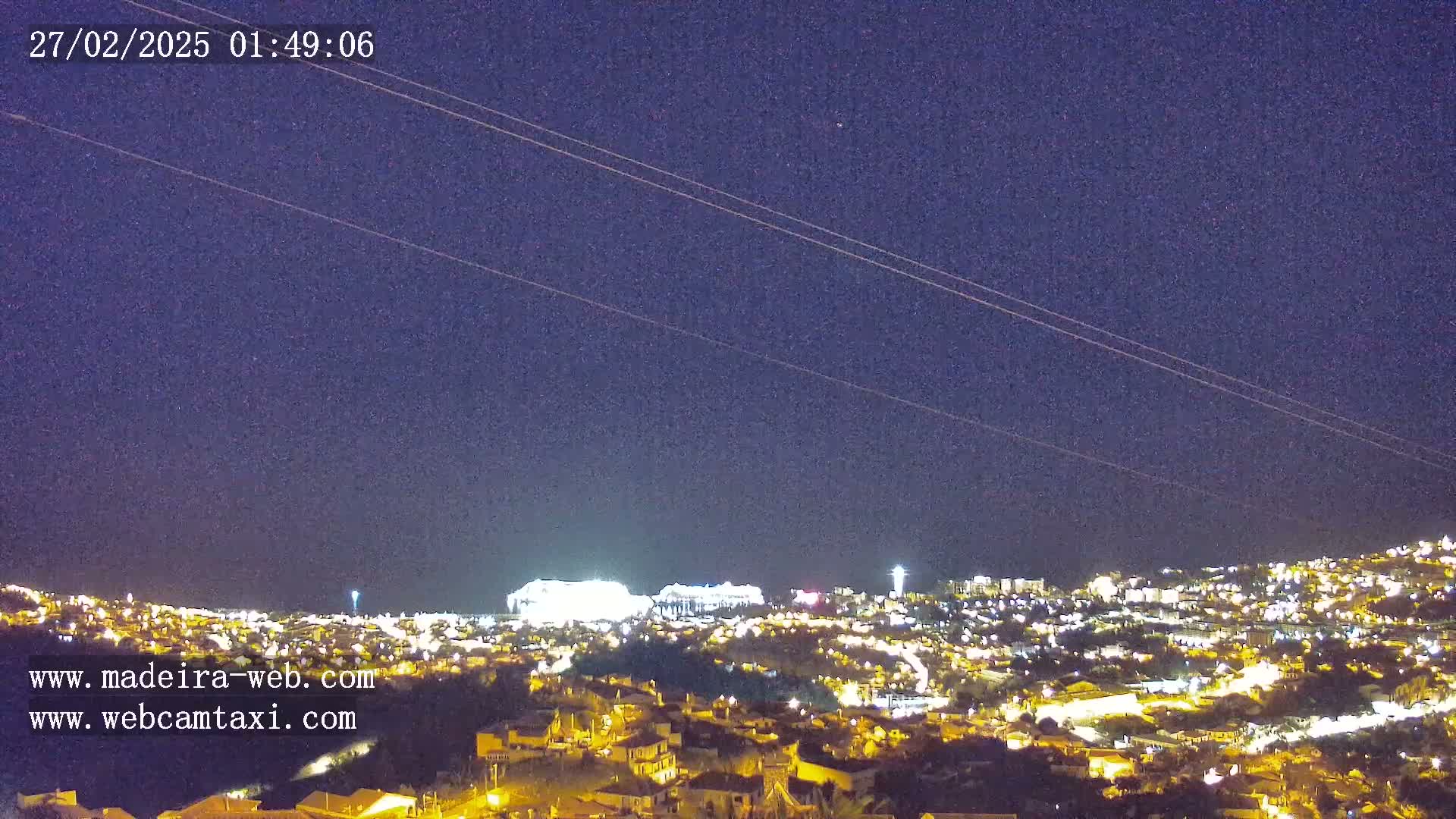 A nighttime view of a city illuminated by lights, under a clear, dark sky with power lines visible across the top.