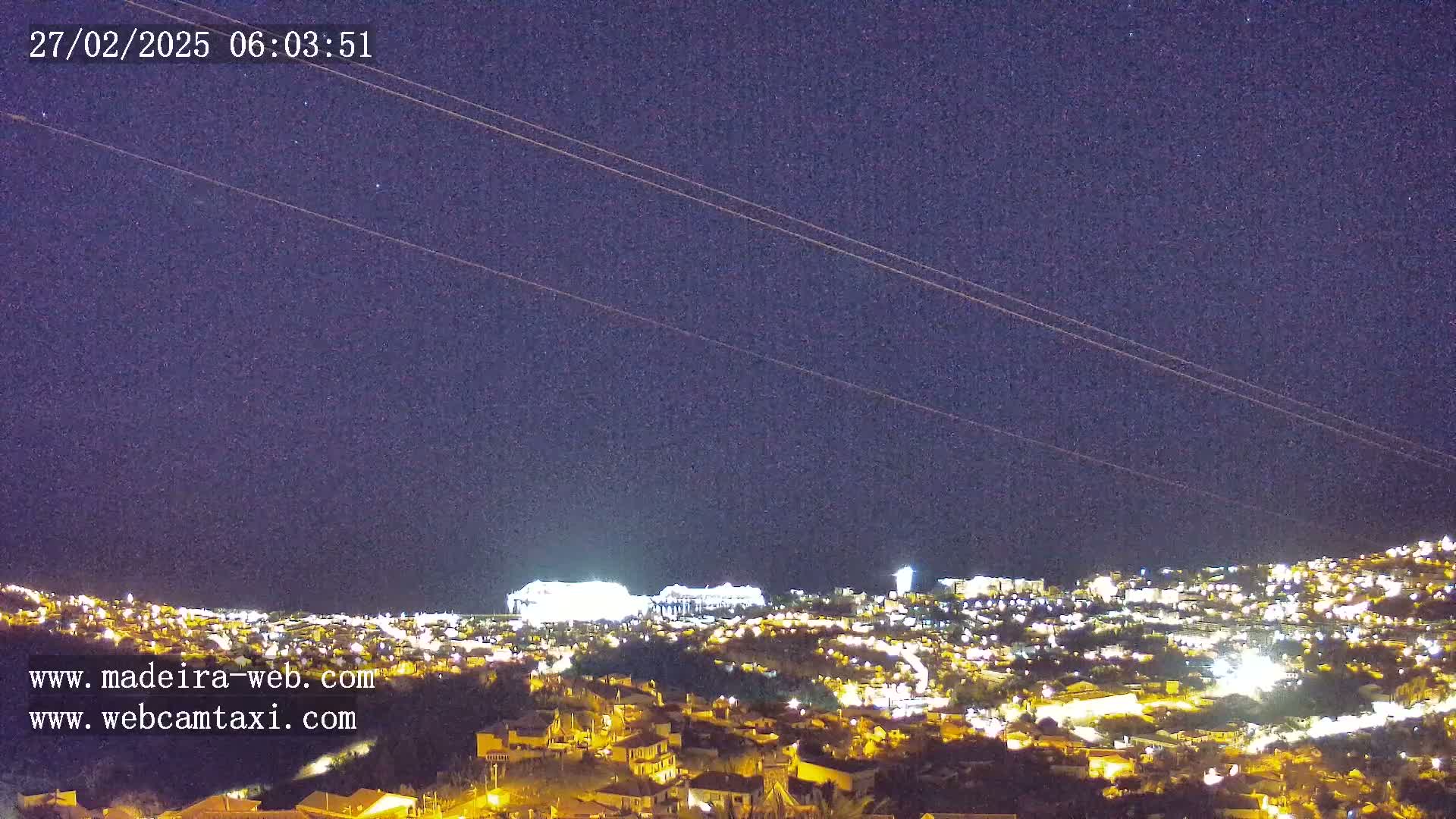 A nighttime view of a city illuminated by lights under a clear, dark sky with a few stars visible.