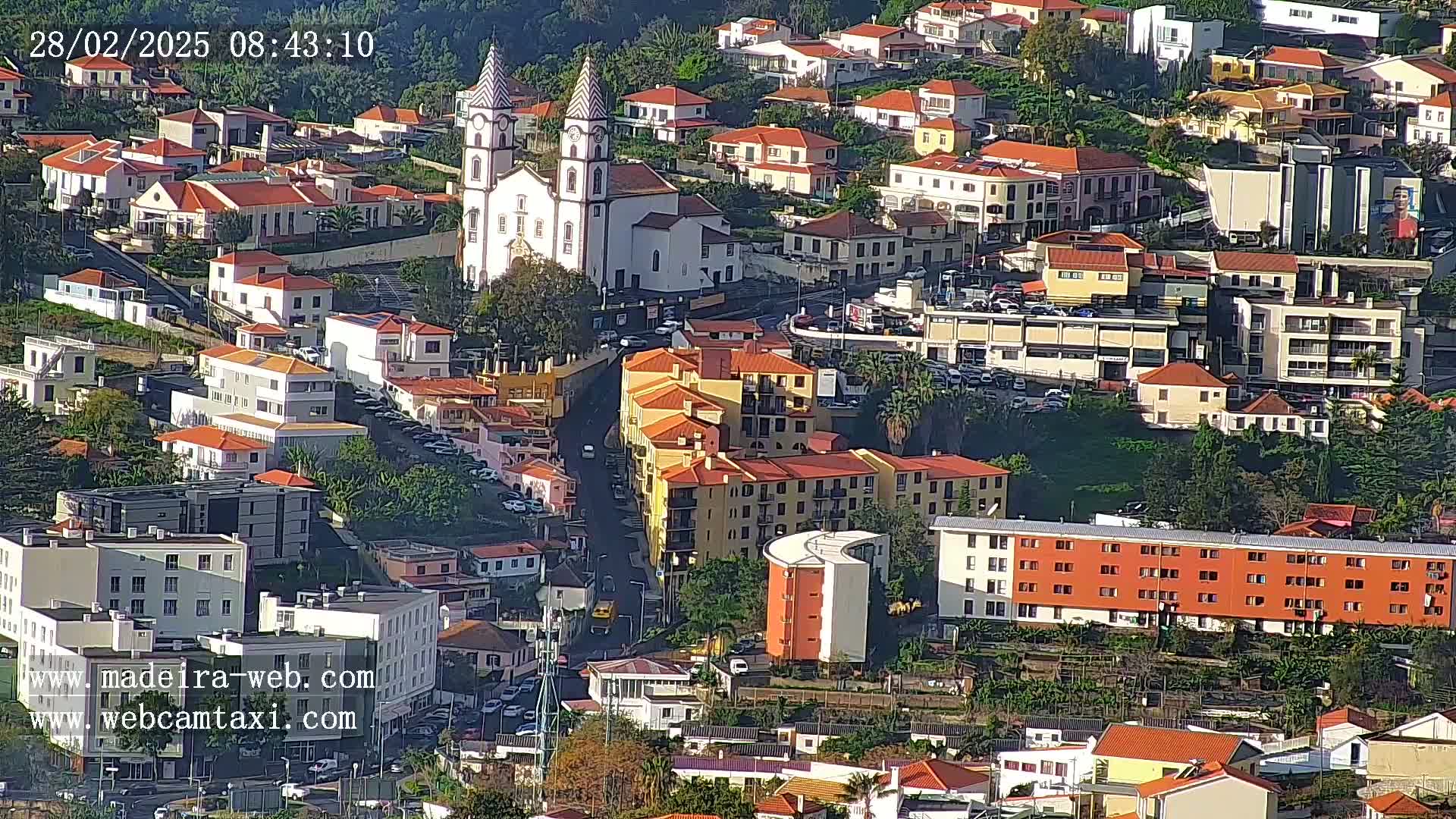 A hillside town with many low-rise buildings, including a church with twin towers, is seen under sunny conditions.