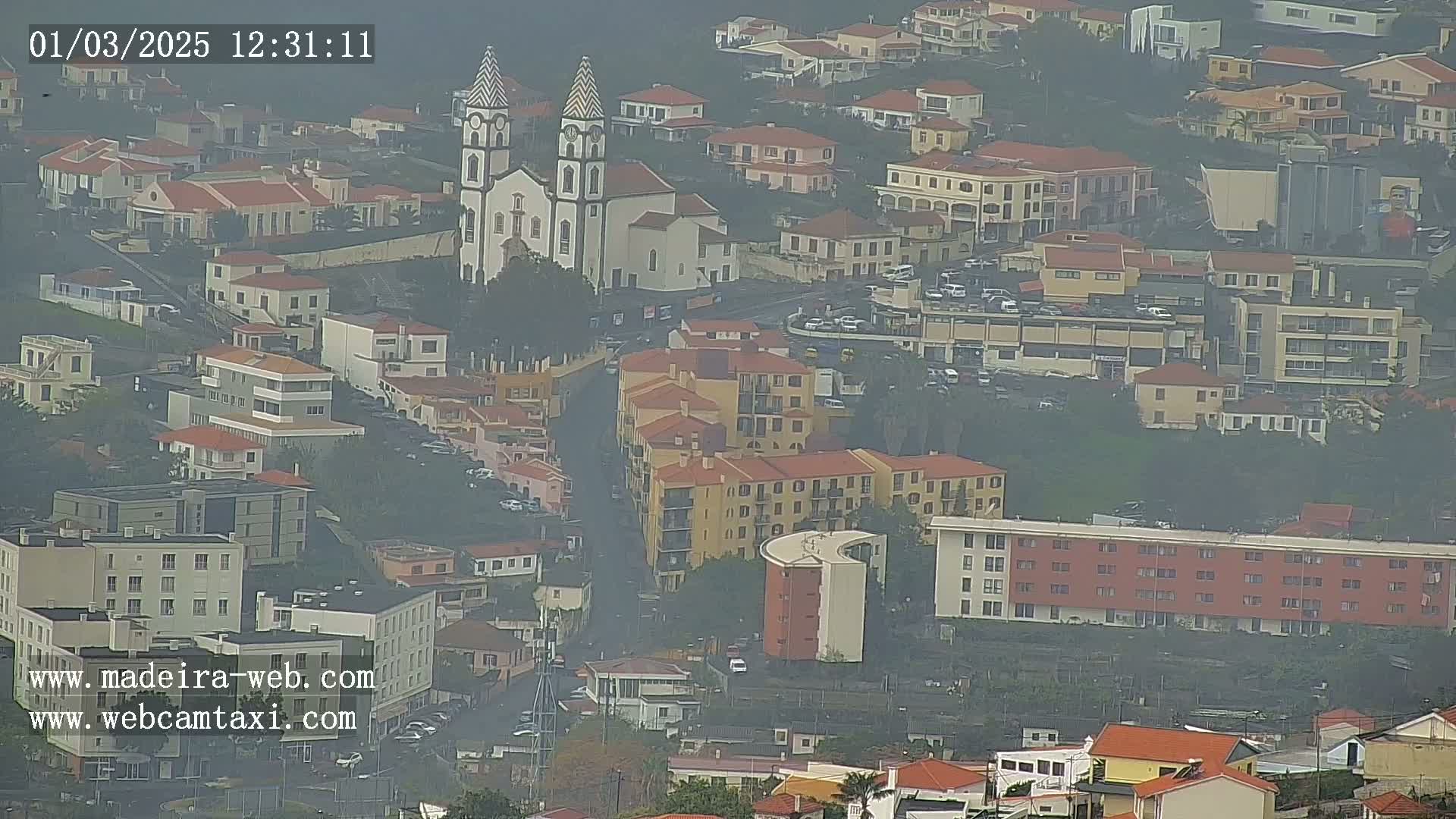 A hazy view of a town, featuring a prominent church and numerous buildings, is seen from above.