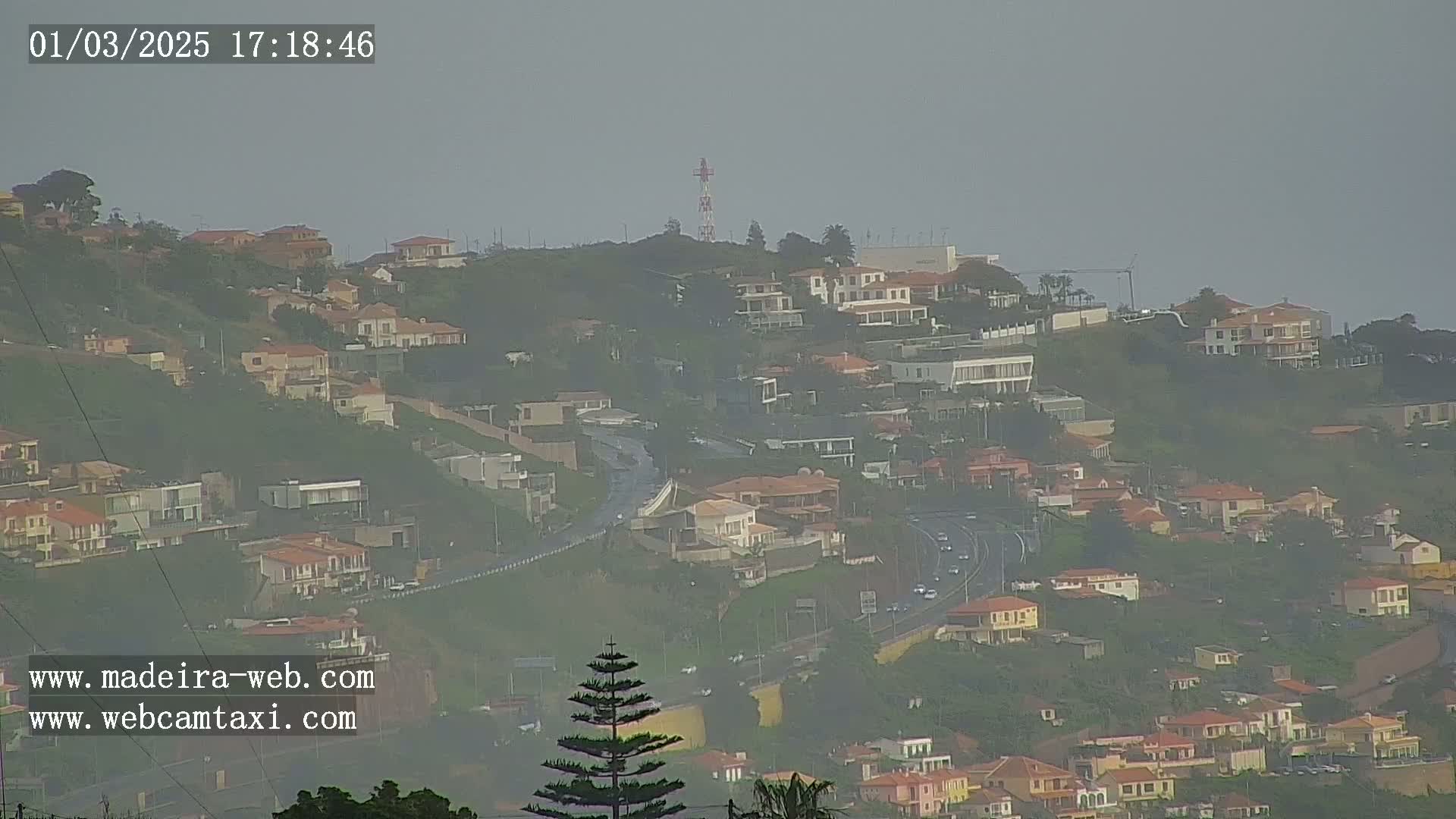 A hazy view shows a hillside covered in houses and a highway, with a communications tower visible in the distance.