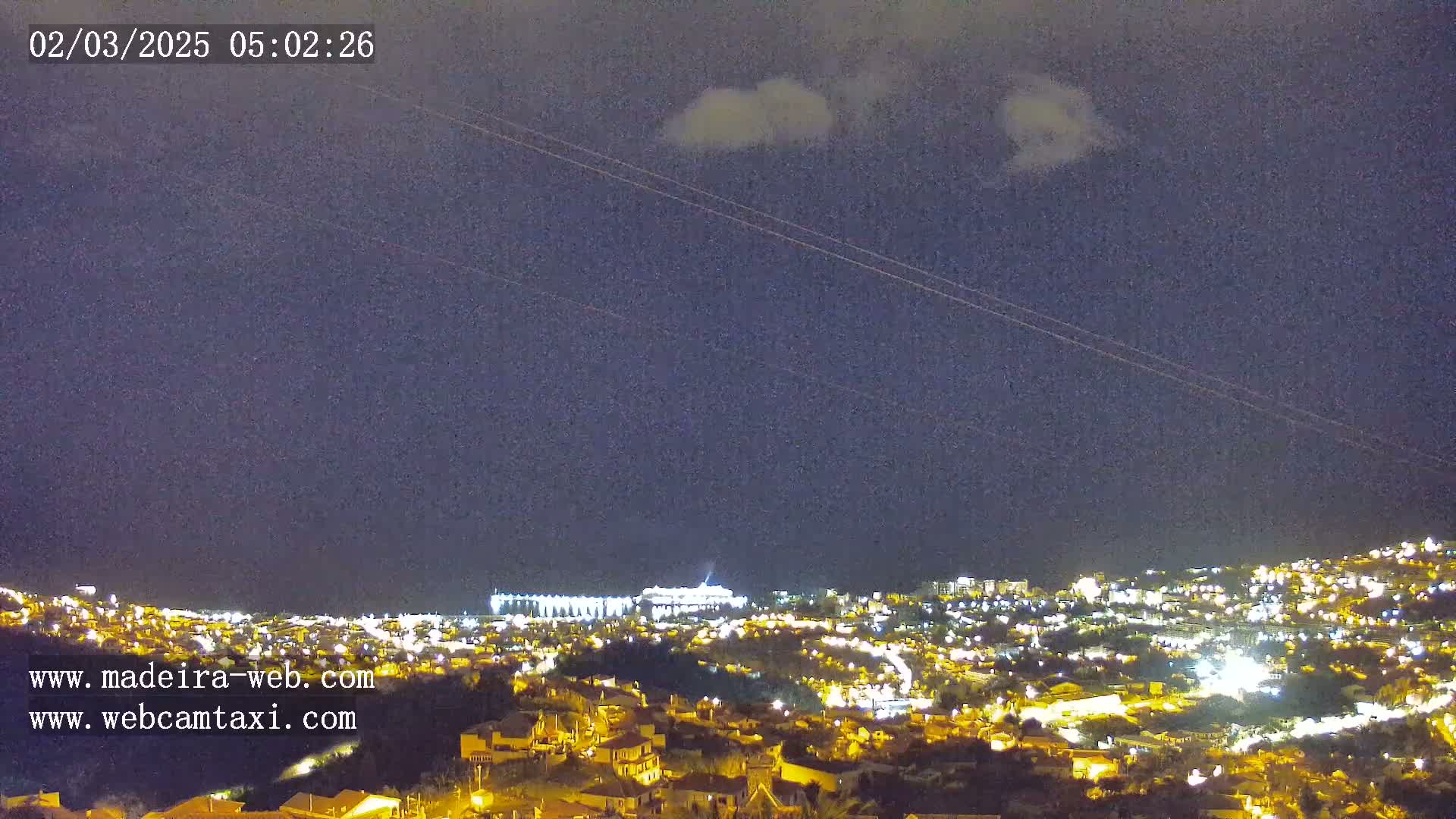 A nighttime view of a brightly lit town nestled below a dark, cloudy sky.