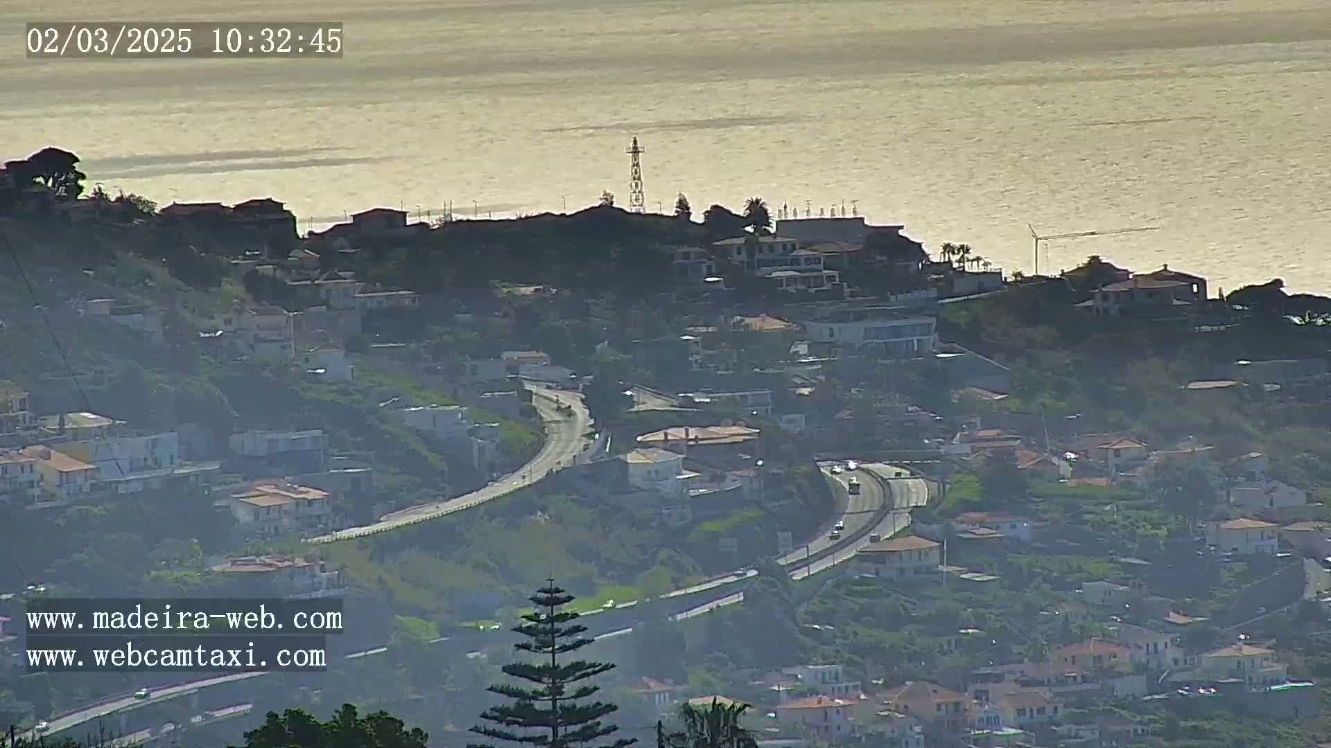 A hazy coastal town with a winding highway overlooking a calm ocean under a bright sky.