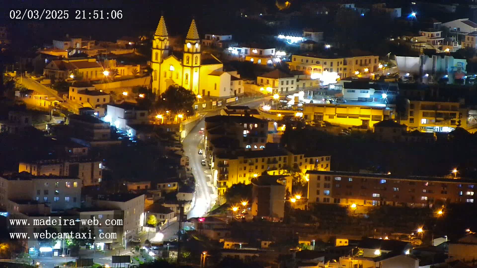 An aerial nighttime view of a town illuminated by streetlights, centered on a brightly lit church.