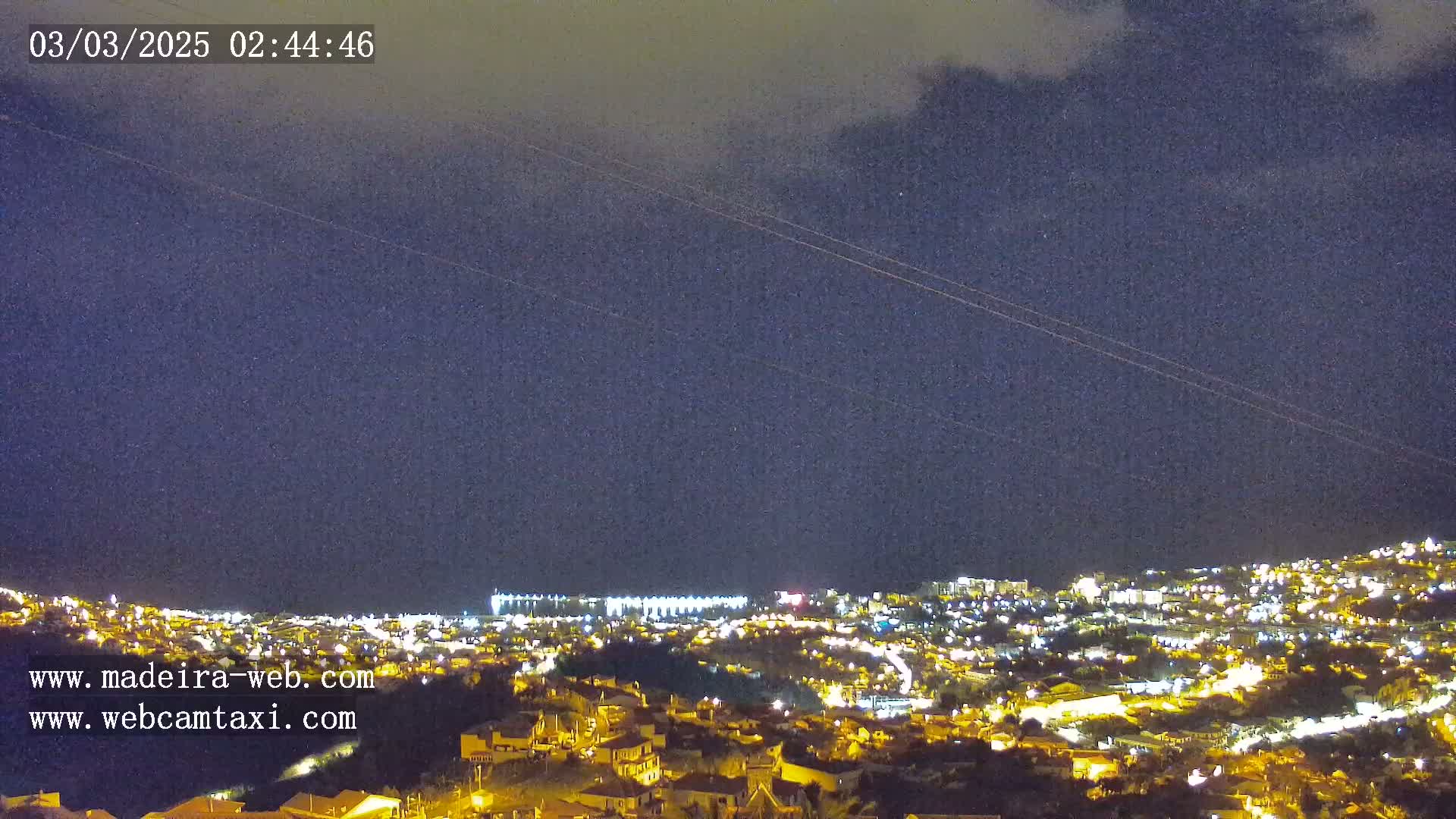 A nighttime view of a city illuminated with lights under a dark, cloudy sky.