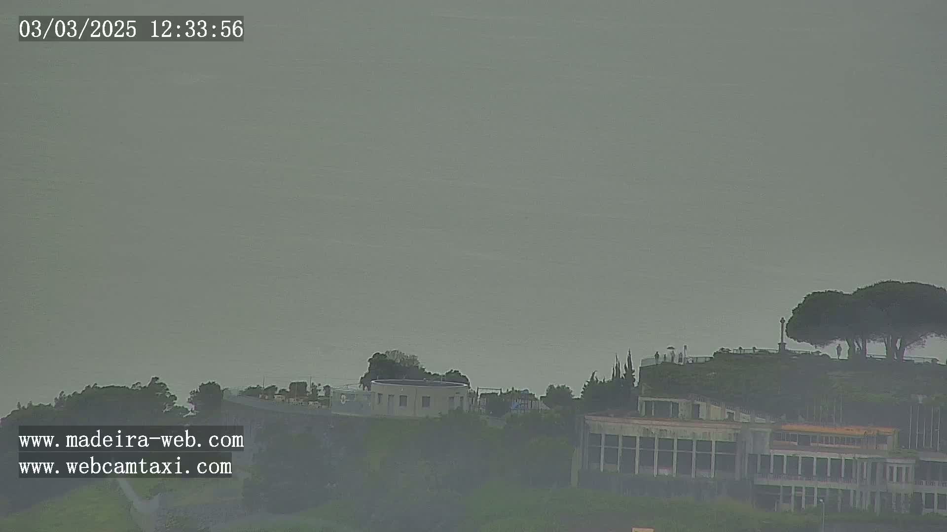 A hazy, overcast day reveals a distant coastline with buildings and trees shrouded in mist.